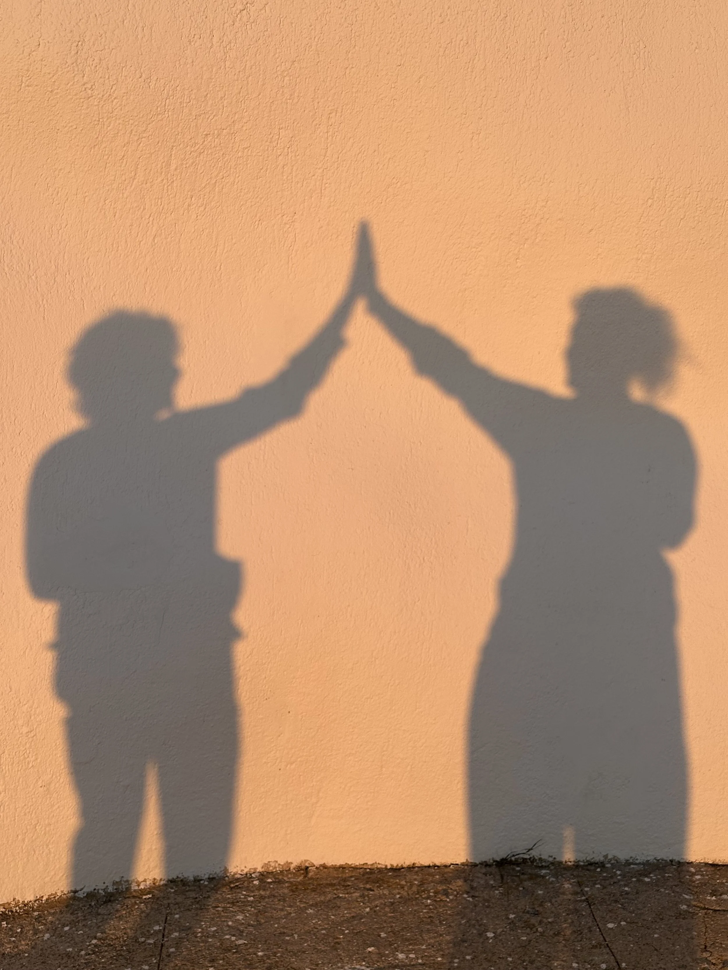 Shadow of two people giving each other a high five against a peach wall.