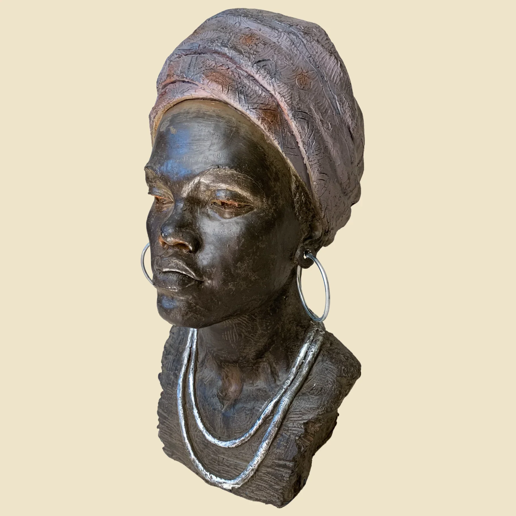 A bronze bust of a woman wearing a headwrap and large hoop earrings, with a necklace, set against a plain background.