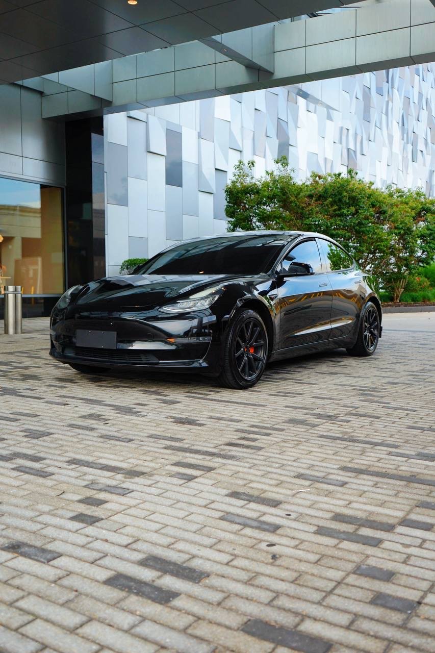 A black tesla car parked on a brick paved area outside a modern building with geometric metal paneling and greenery in the background in Charlotte, North Carolina