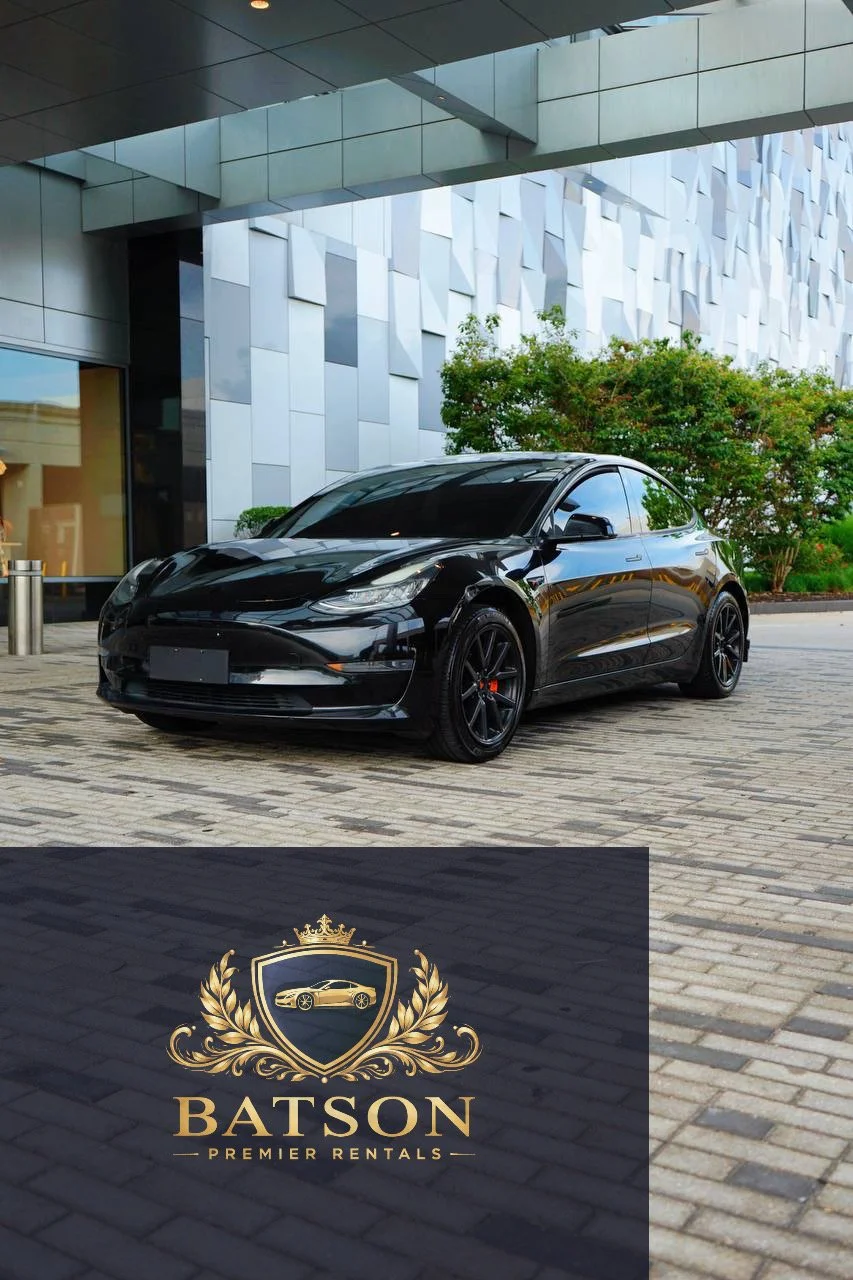 A black Tesla Model 3 parked outside a modern building with glass and metal panels, and greenery nearby, with Batson Premier Rentals logo at the bottom.