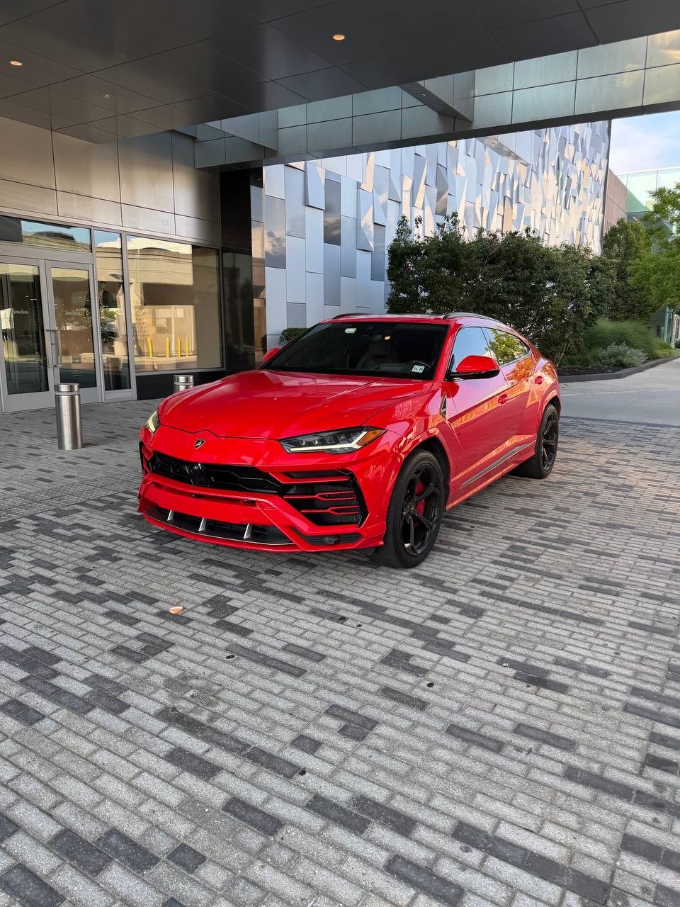 Red Lamborghini Urus parked outside a modern building in Charlotte, North Carolina with glass doors and patterned walls.