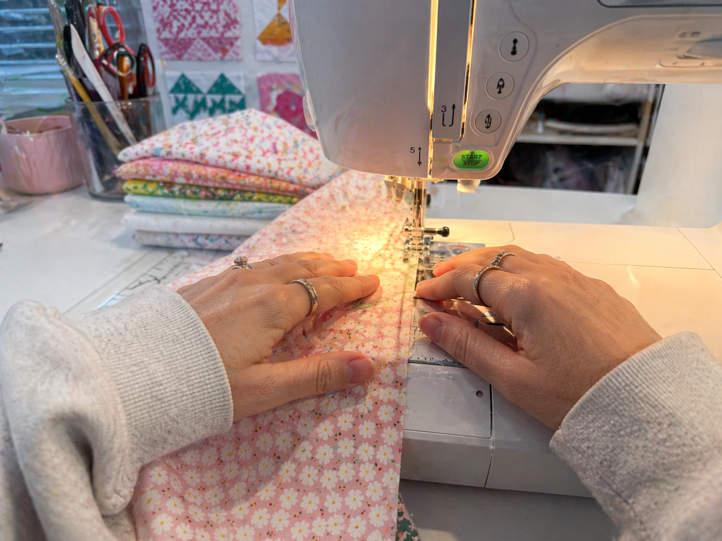 A person sewing fabric on a sewing machine, with colorful fabric pieces and quilting projects in the background.