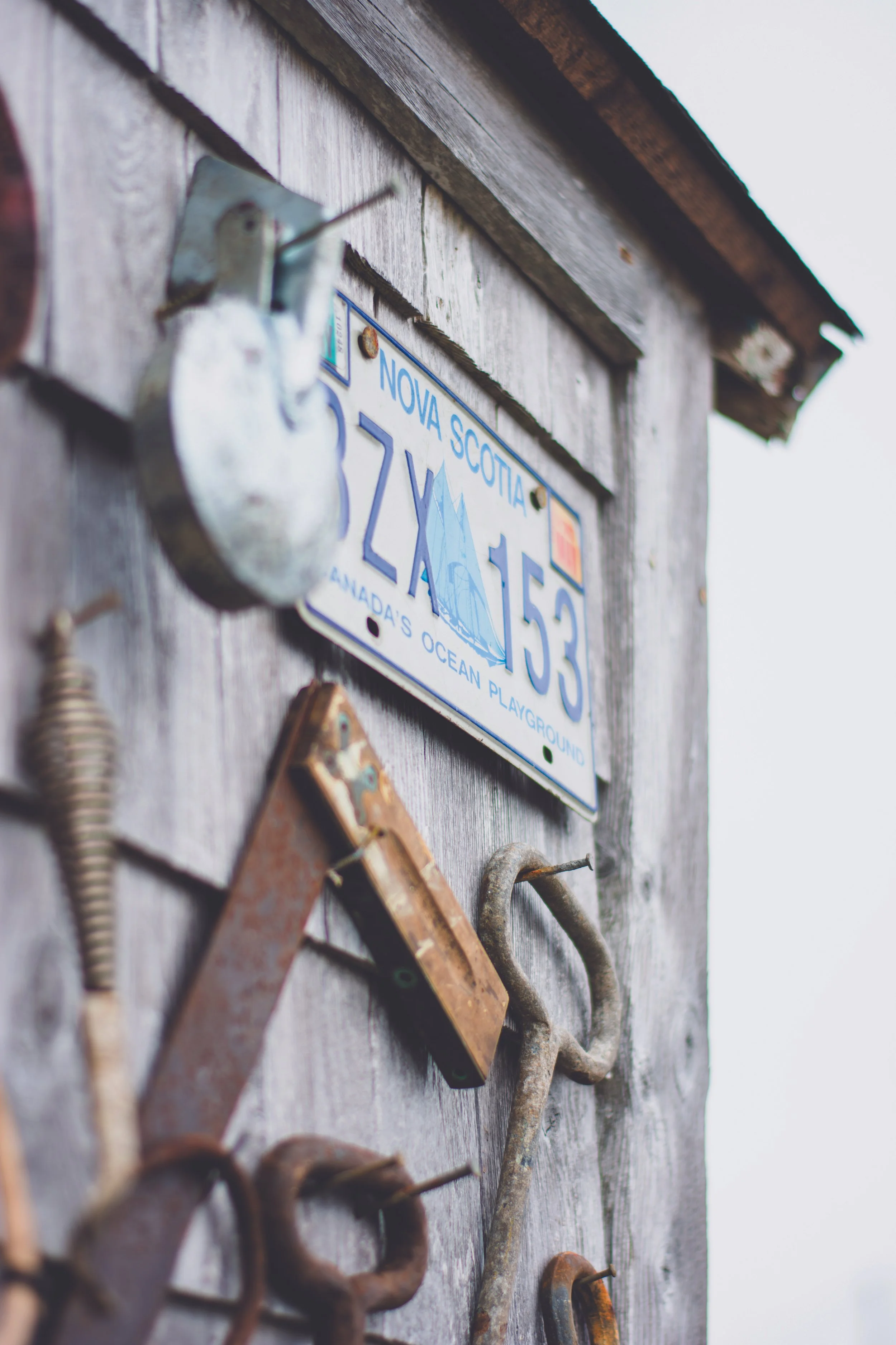 Close-up of a weathered wooden wall with vintage tools and a Nova Scotia license plate, featuring a sailboat illustration.
