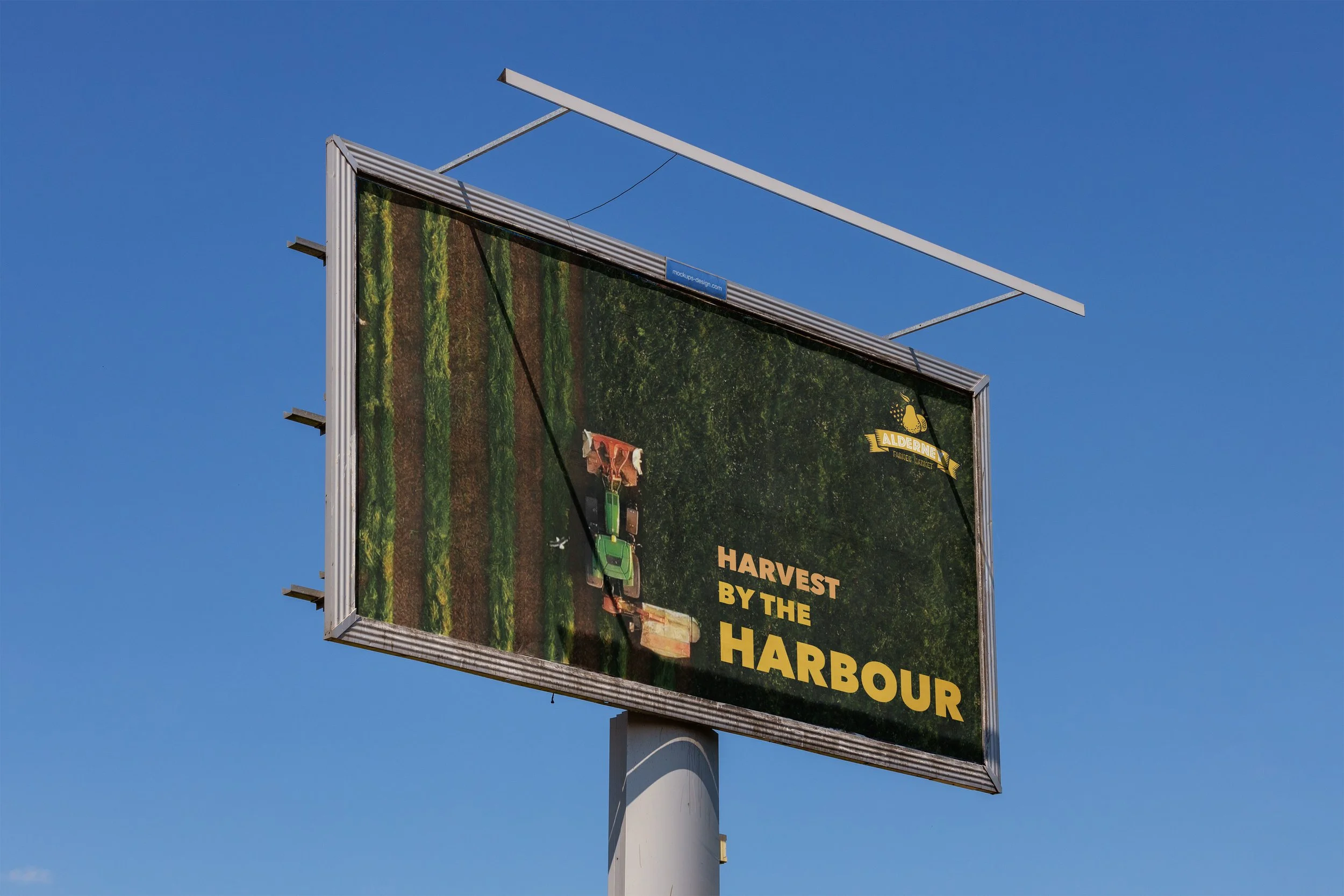 Billboard advertisement with an image of a tractor and crop fields, promoting harvest activities by the harbor for Alderney.