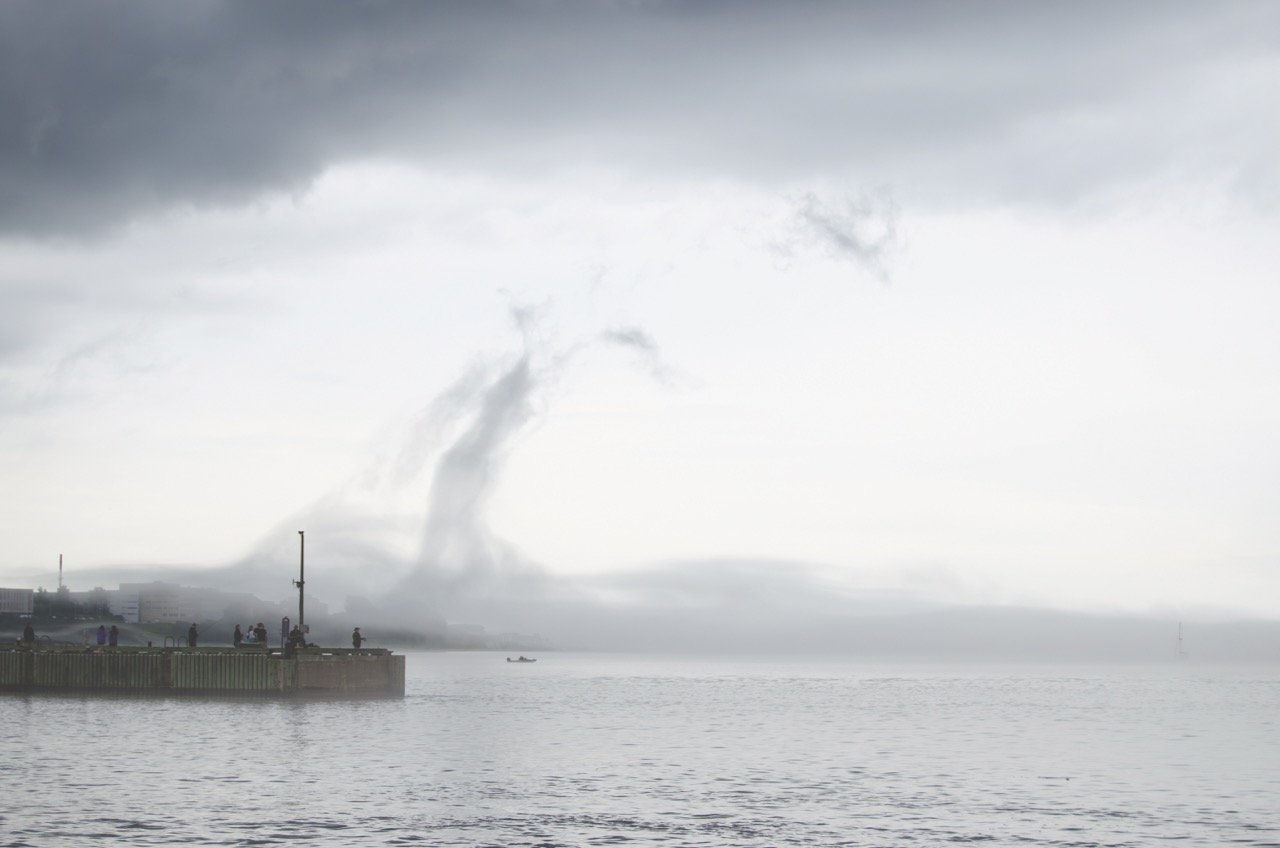 Dark storm clouds over a body of water with a tornado forming in the distance.