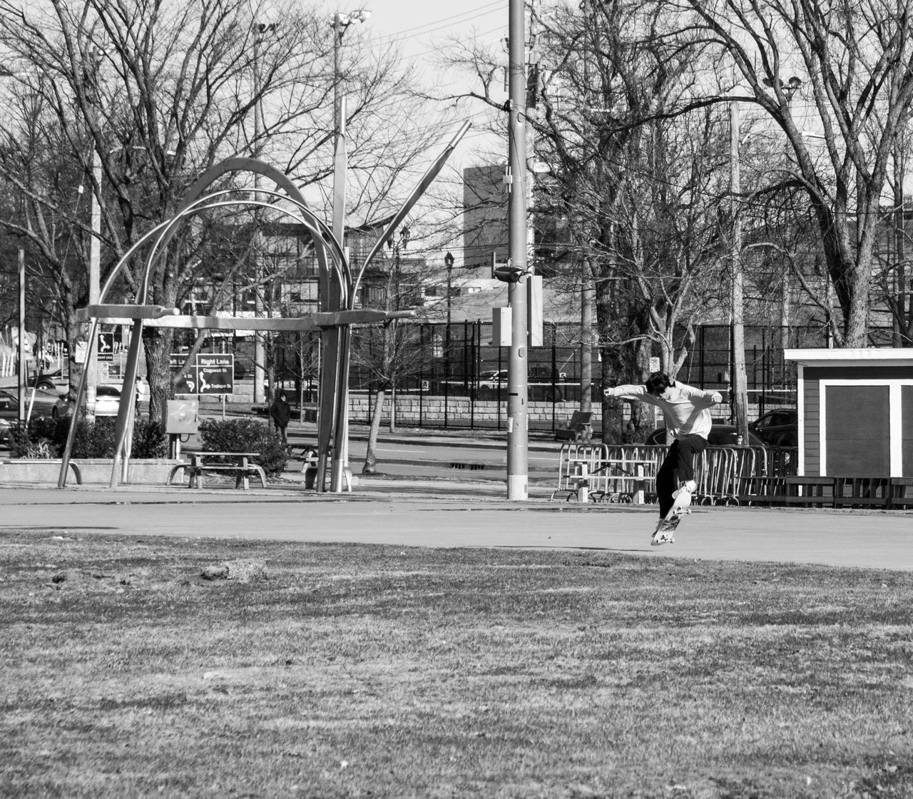 A person skateboarding on a paved area in a park with trees and a cityscape in the background.