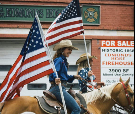 Sierra rides confidently in the arena carrying the American flag, showcasing patriotism, horsemanship, and the spirit of rodeo competition. This moment captures the connection between rider and horse while honoring tradition.