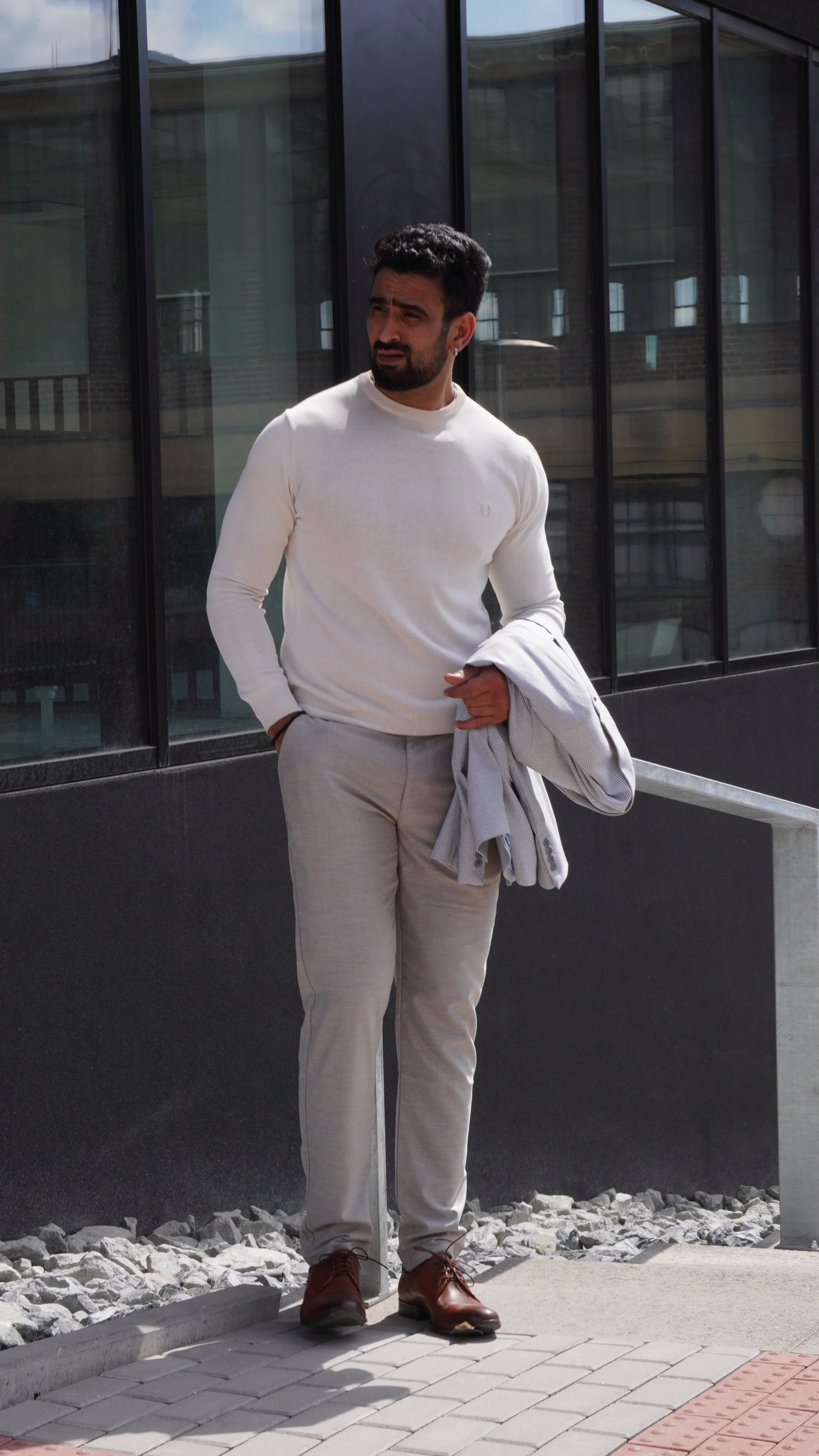 Muž ve světlém svetru a kalhotách s přehozeným sakem představuje moderní pánský smart casual styl pro každý den od MEEMA Plzeň.