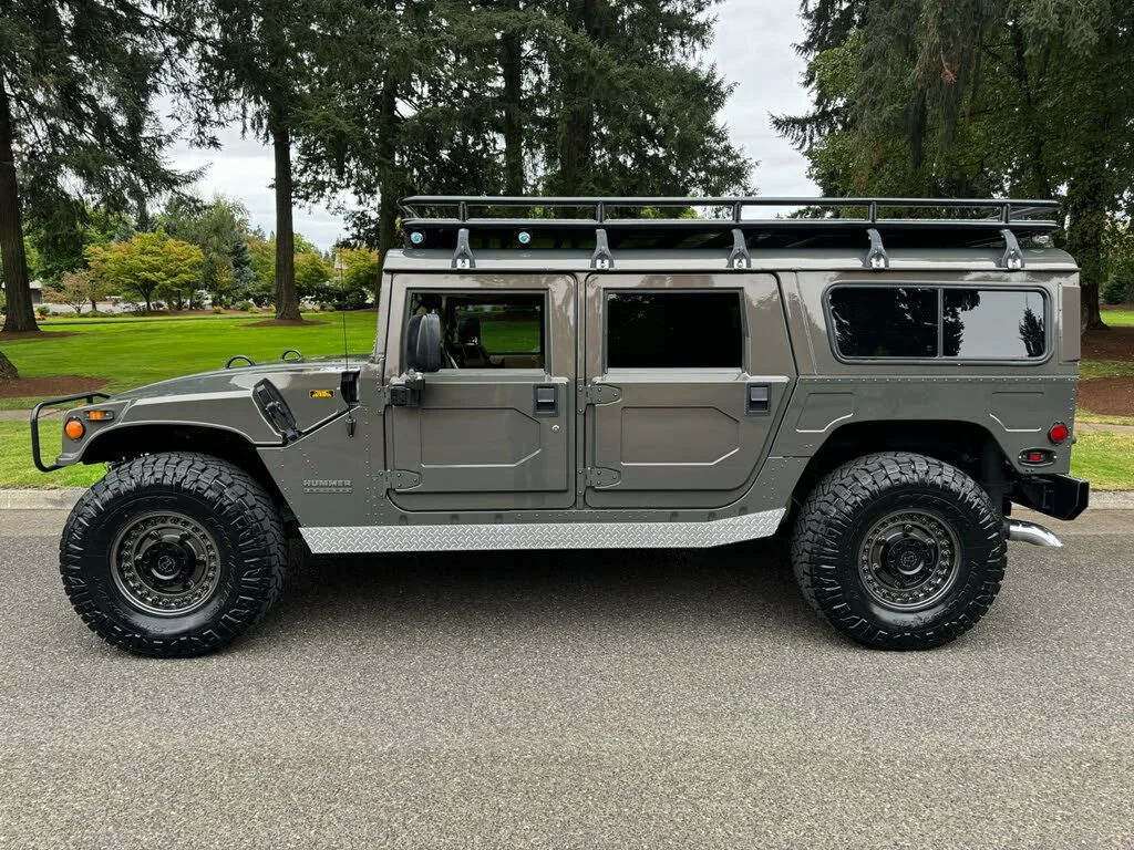 Gray SUV with off-road tires, roof rack, and tinted windows parked on a paved road with trees in the background.
