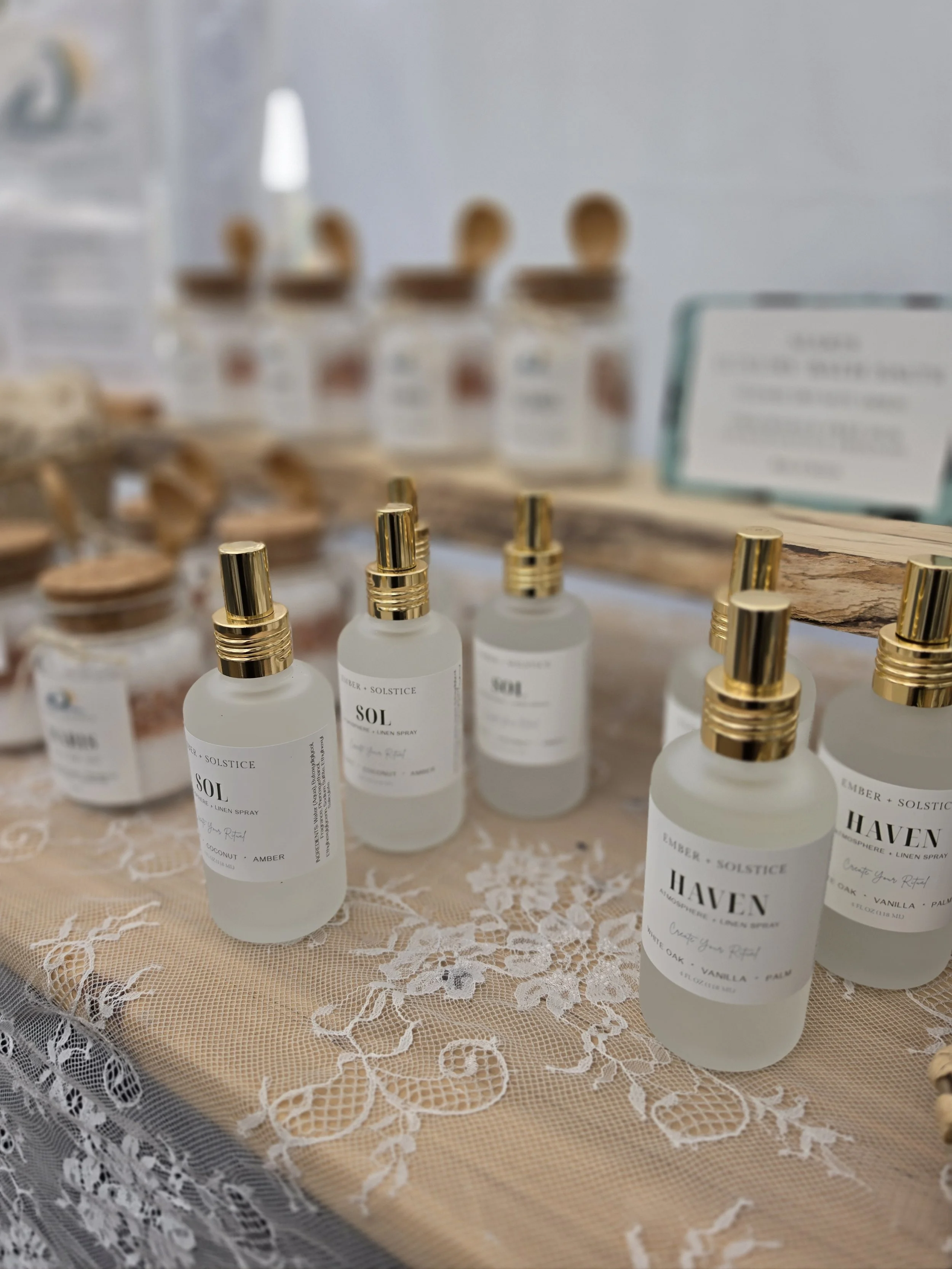 Various white spray bottles with gold caps labeled 'Haven' on a lace-covered table.