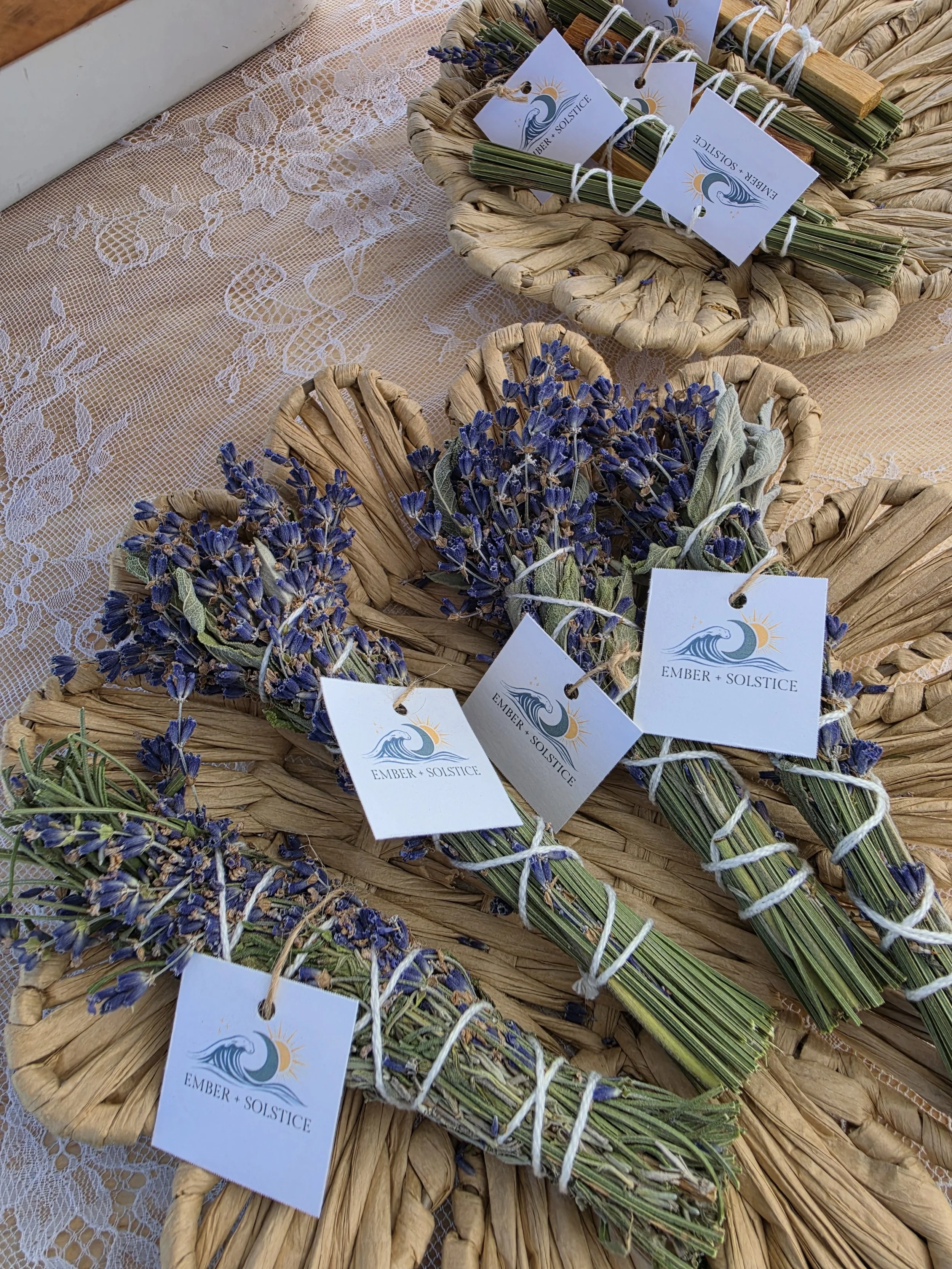 Sprigs of dried lavender tied with white string and attached to small white tags with a logo and the text "Ember + Solstice" on a lace tablecloth.
