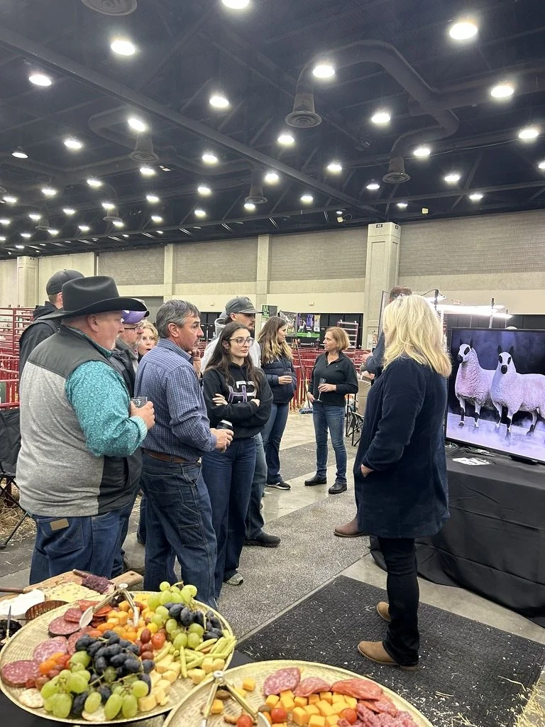 Group of people listening to Tracy BLoom at NAILE, at a presentation with screen showing images of sheep, table with fruit and meat in the foreground, at an indoor event space.