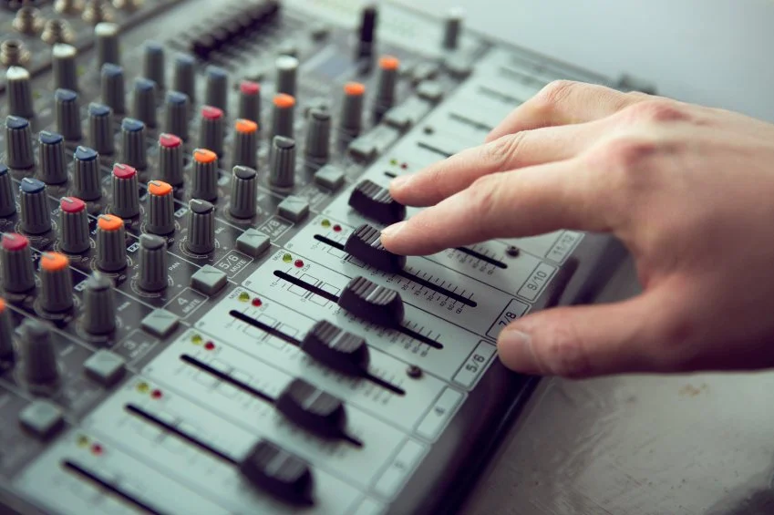 Close-up of a person's hand adjusting controls on an audio mixing console with various sliders and knobs.