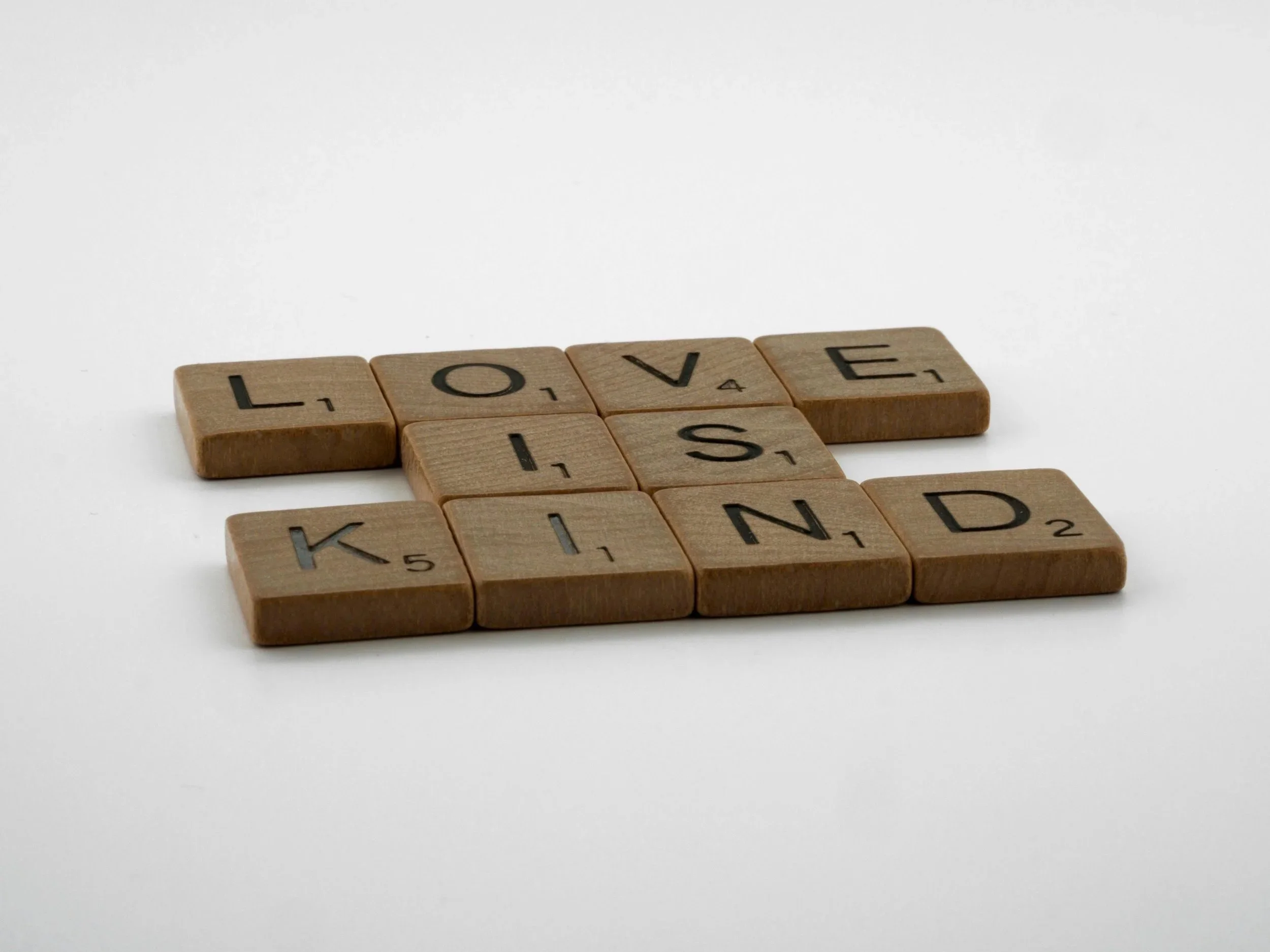 Scrabble tiles spelling out 'LOVE,' 'KIND,' and 'KISS' on a white background.
