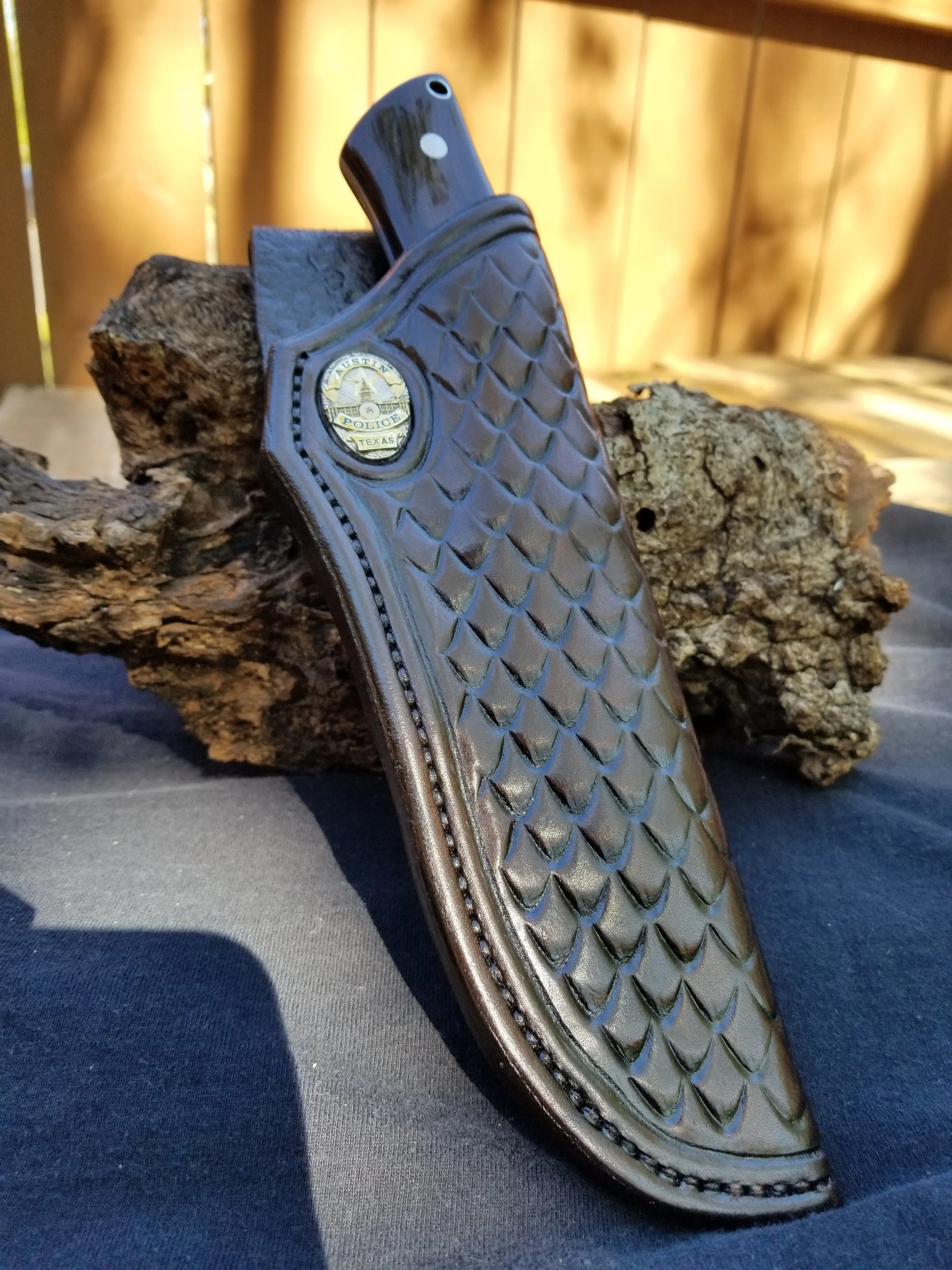 A black leather gun holster with a Texas police badge emblem, resting on a piece of wood outdoors.