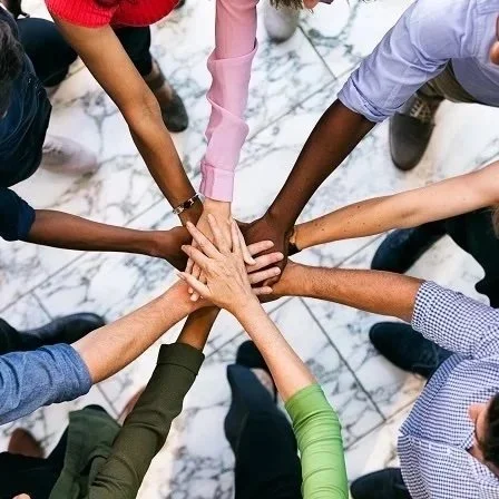 Several diverse people are placing their hands together in a circle, symbolizing unity and teamwork.