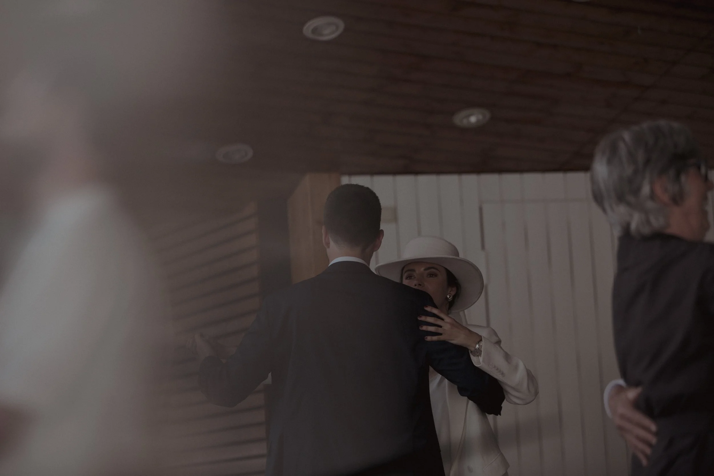 Woman wearing a white hat and white suit dancing with a man in a black suit at an indoor event.