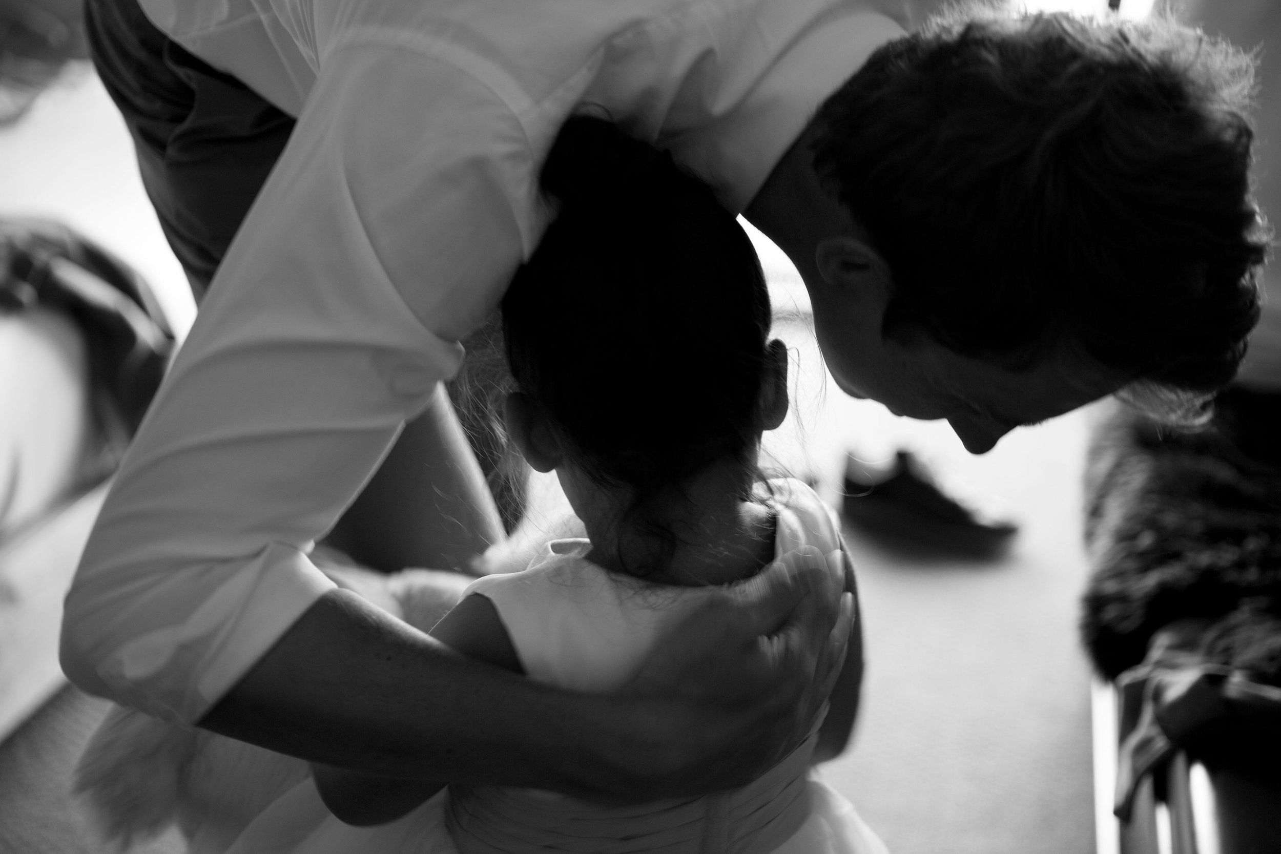 An adult man and young girl sharing a tender moment, with their foreheads touching in an intimate gesture, in a softly lit room.