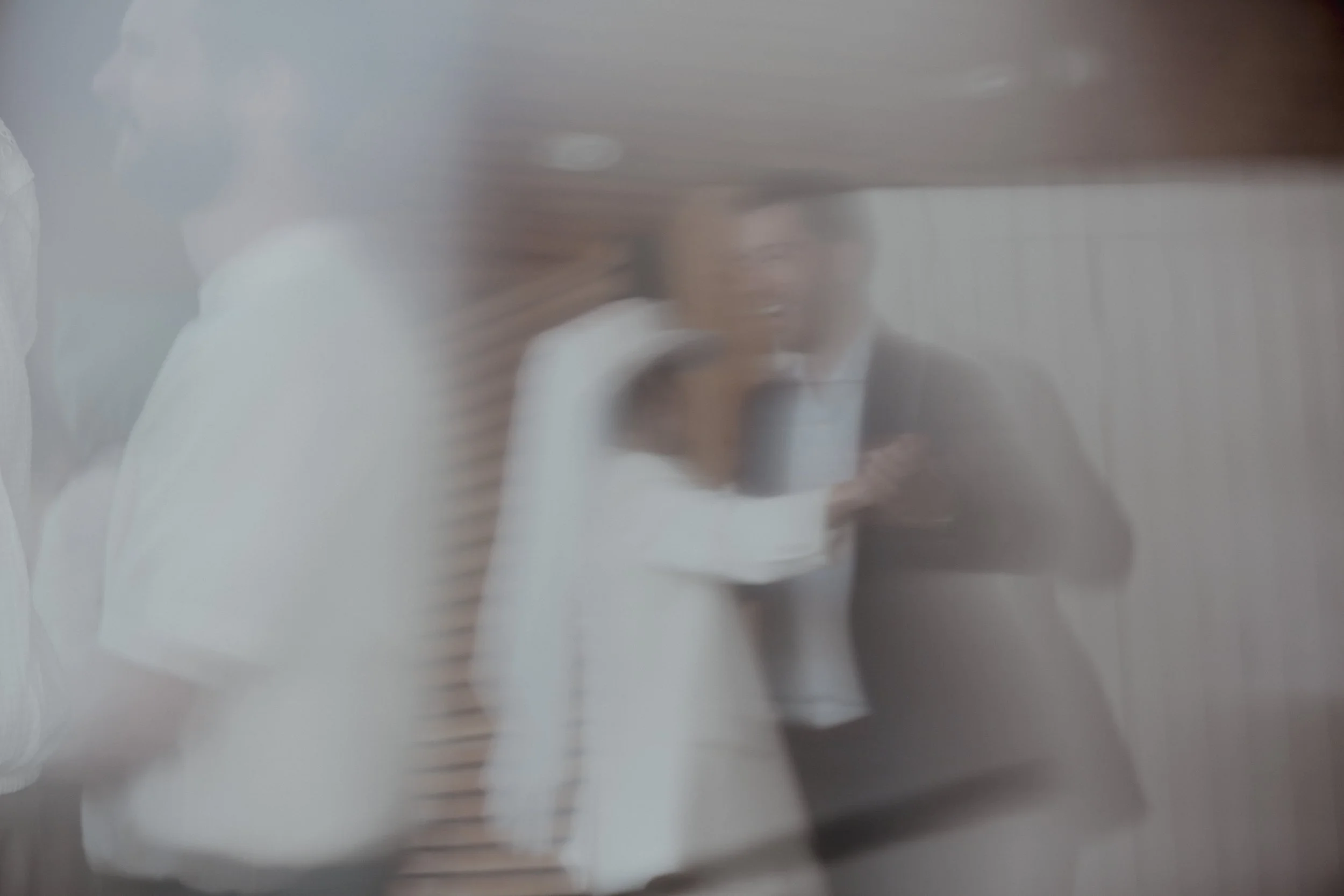 A blurry photograph of a woman in business attire, covering her face with her hand, seen through a scratched or dirty glass.