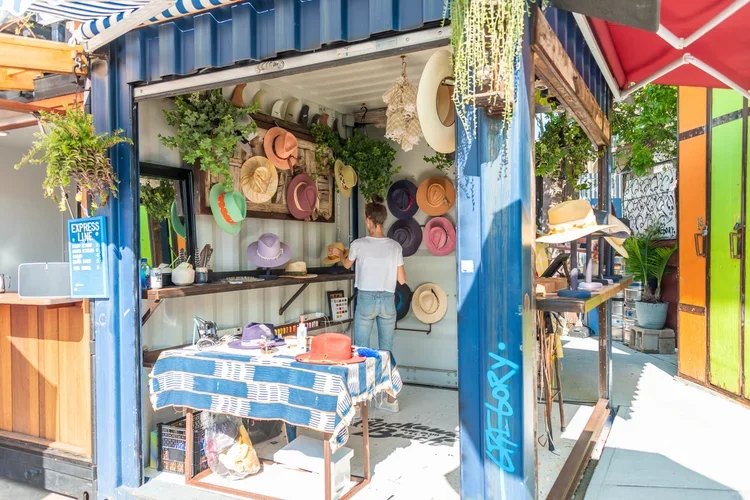 A person shopping for hats at a colorful outdoor market stall with various hats displayed on the wall and shelves.