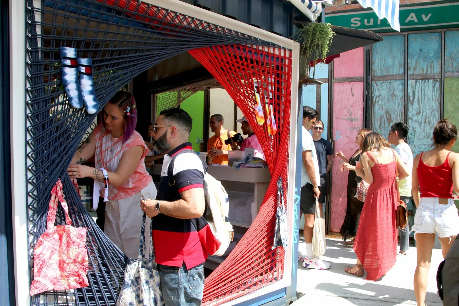 Crowd of people at an outdoor shop with colorful walls and a green street sign reading "Sun Ave" in the background.