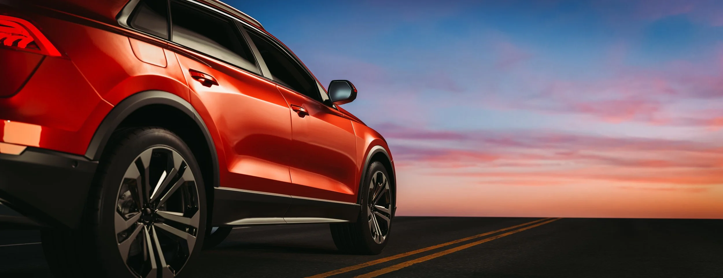 A red SUV parked on a deserted road at sunset with a colorful sky overhead.