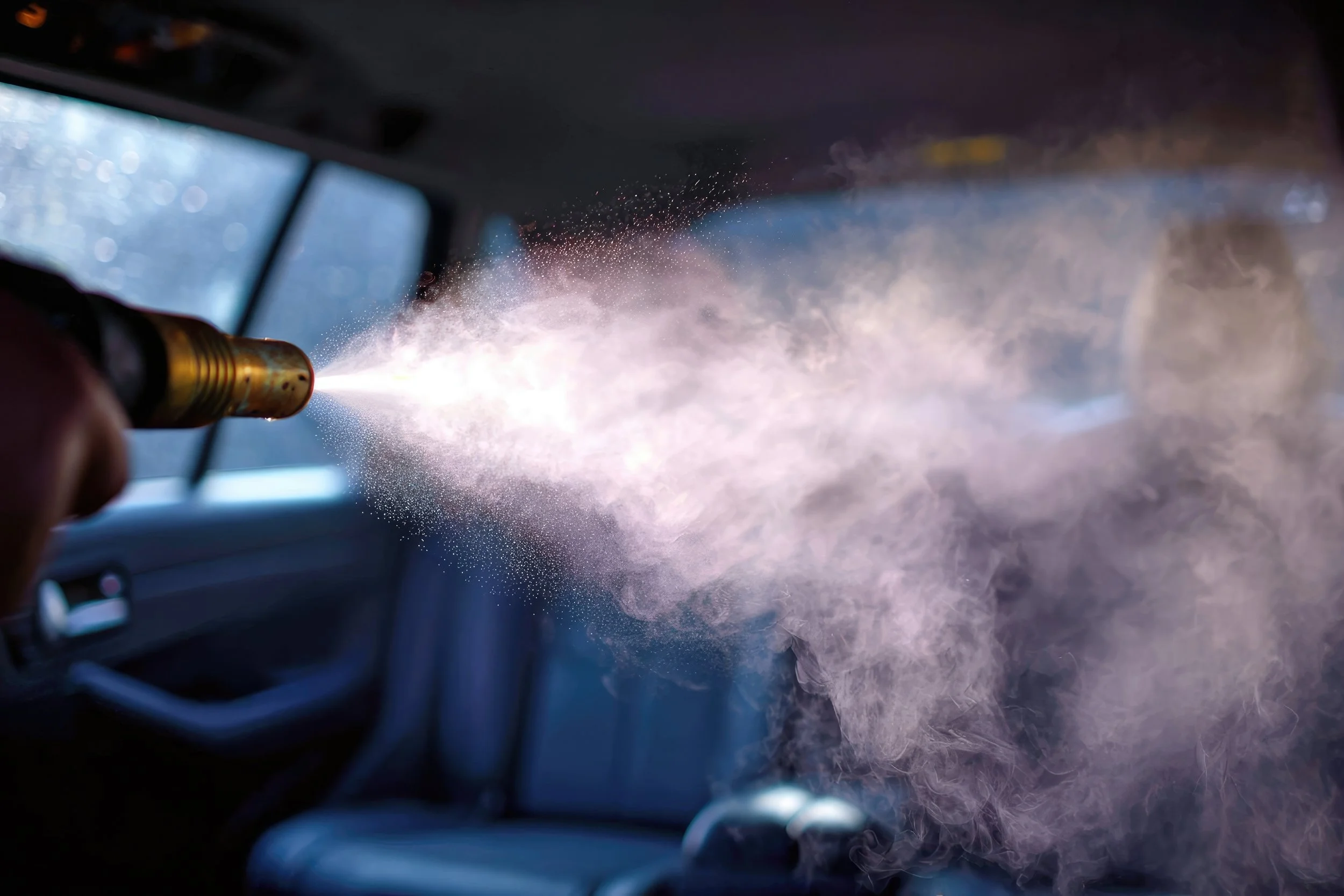 A person using a spray gun inside a vehicle, releasing a burst of spray or mist.