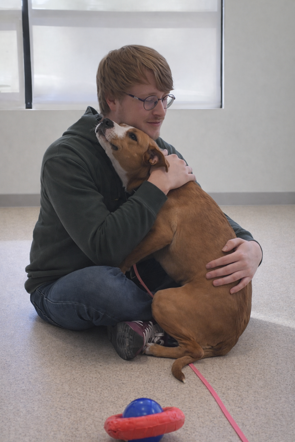 A man sitting on the floor and hugging a brown and white rescue dog..