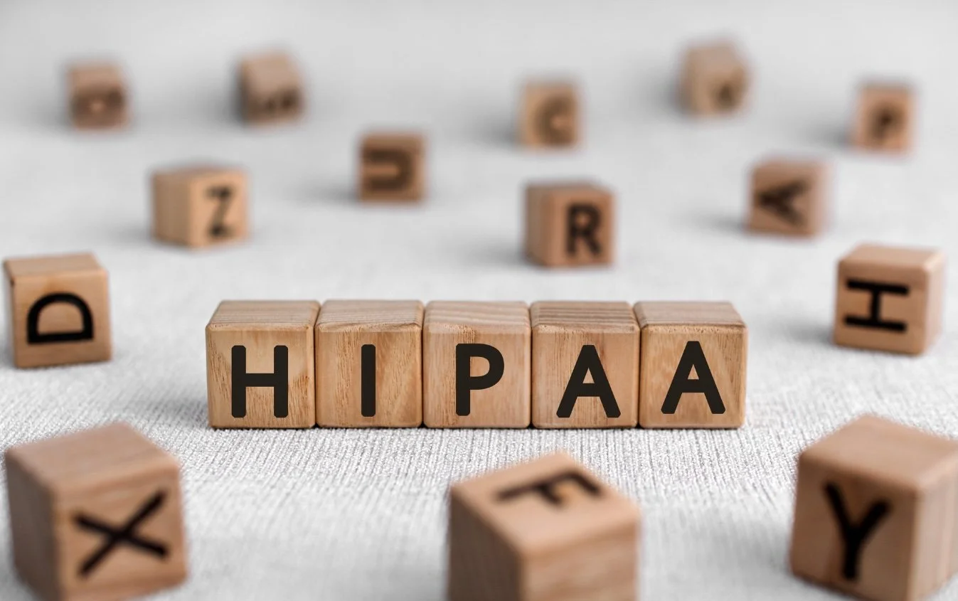 Wooden letter blocks spelling HIPAA on a white surface, with other blocks scattered around.