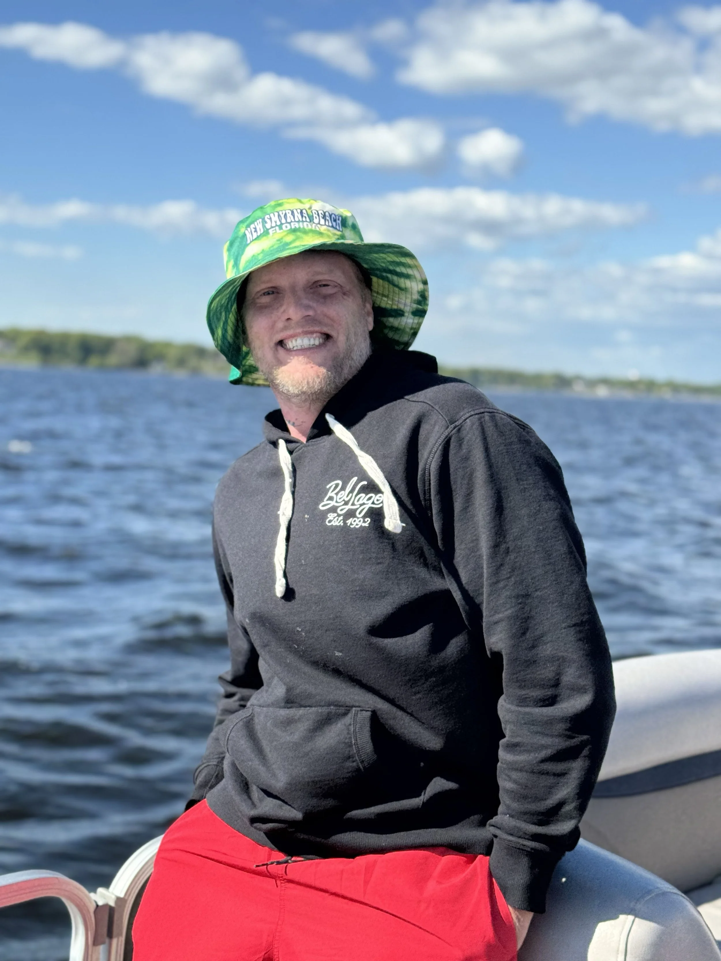 A smiling man standing on a boat with water and a blue sky with white clouds in the background. He owns the company lawnable. He loves operating a bobcat in the Grand Rapids, Michigan and surrounding areas.