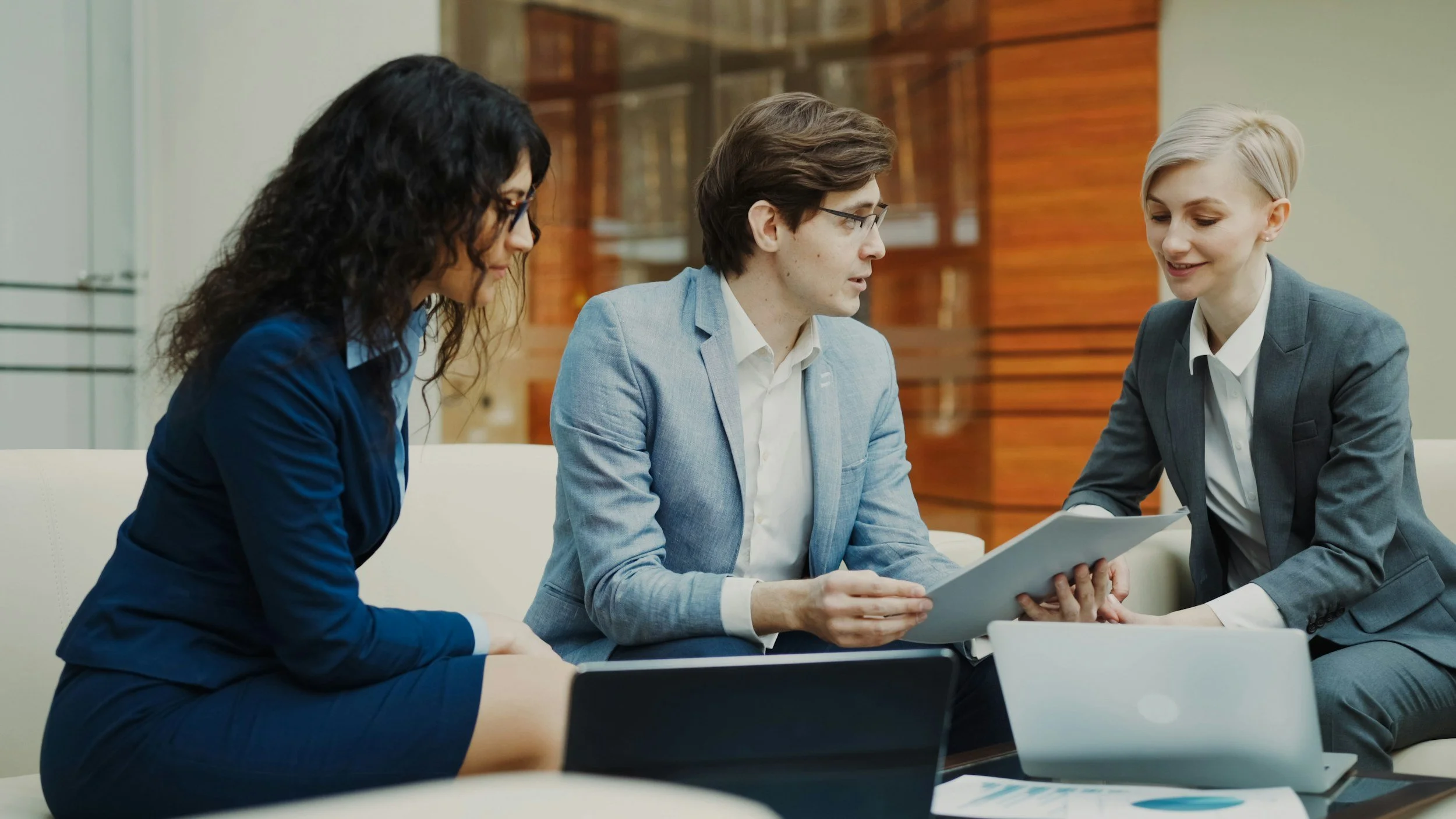 Three business professionals having a meeting in a modern office, with laptops and documents on the table.
