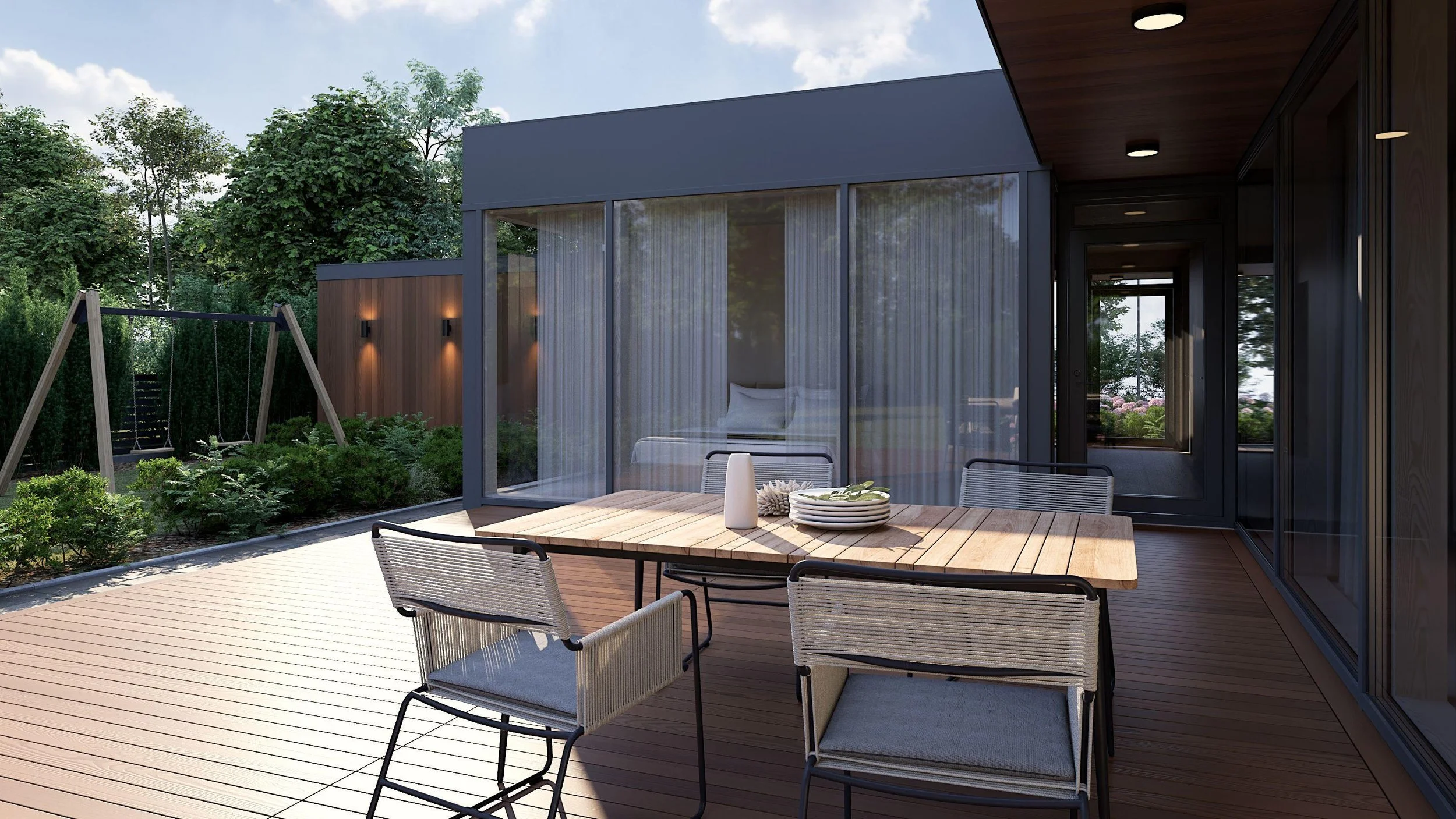Modern outdoor patio with wooden deck, dining table with chairs, glass-enclosed bedroom with sheer curtains, swing set in garden, surrounded by greenery and trees, under a partly cloudy sky.