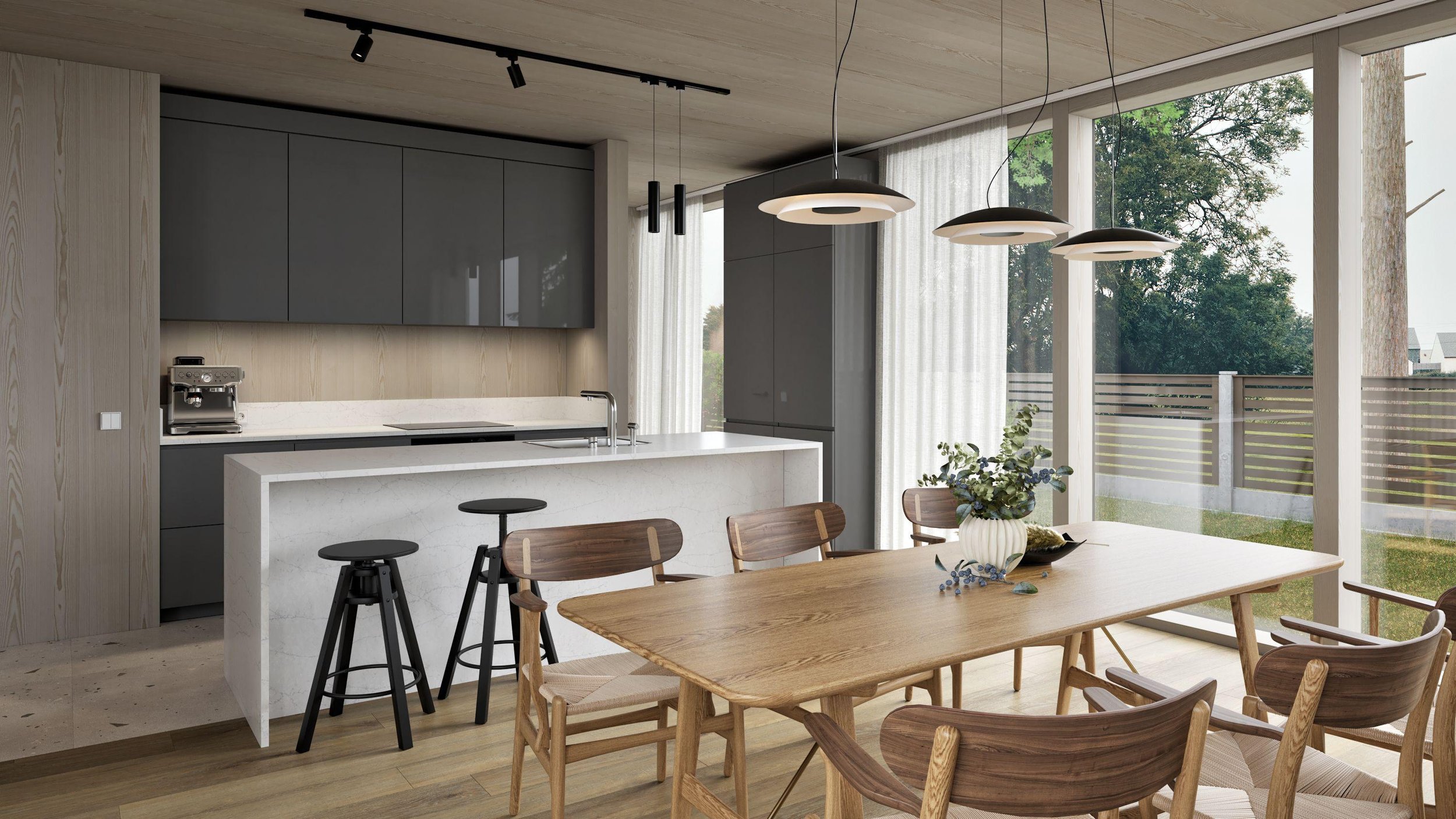 A modern kitchen and dining area with large windows showing trees and a wooden fence outside. The kitchen has gray cabinets, a white marble island with a sink, and a coffee machine. The dining table is wooden with chairs, and a vase of flowers is placed on it. Pendant and track lighting hang from the ceiling.