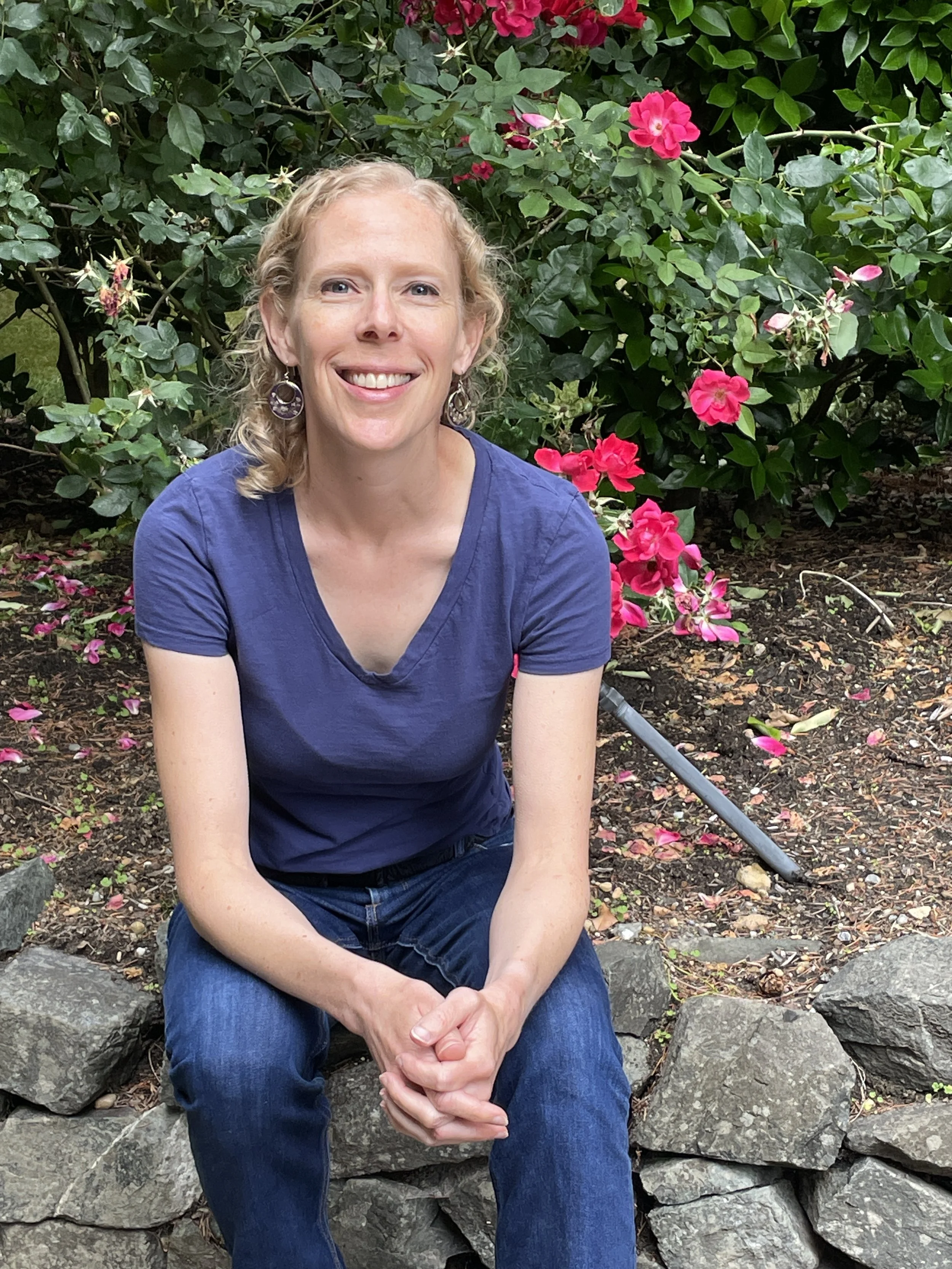 The founder of Elevation Provider Wellness physician burnout coaching sitting on a rock wall with flowers in the background.