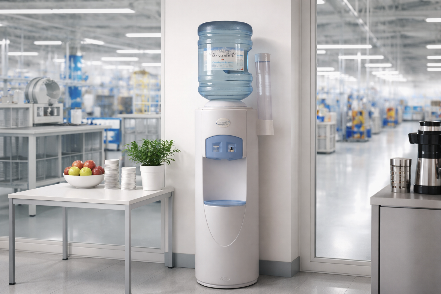 Wasserspender mit Wasserbehälter, daneben eine Tafel mit Äpfeln und eine Pflanze in einem weißen Topf, in einer Büroumgebung.