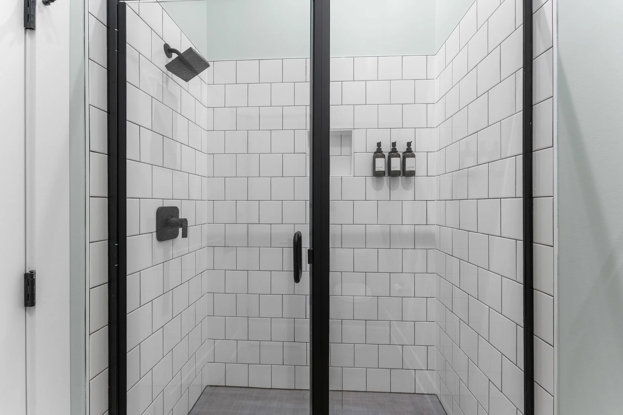 A modern shower with black fixtures, white tile walls, and a glass door.