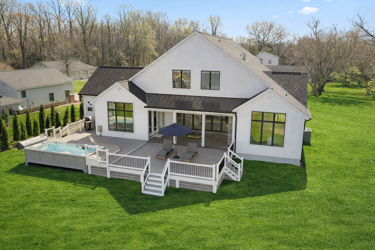 Modern white house with large windows, a spacious backyard deck with outdoor furniture, and a 17 ft long swim spa.