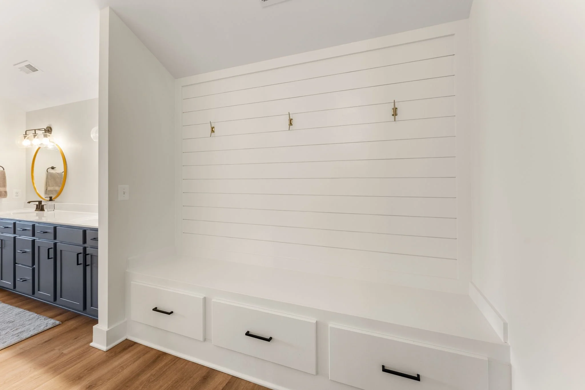 White built-in bench with three drawers and hooks on a shiplap wall in a modern bathroom area.