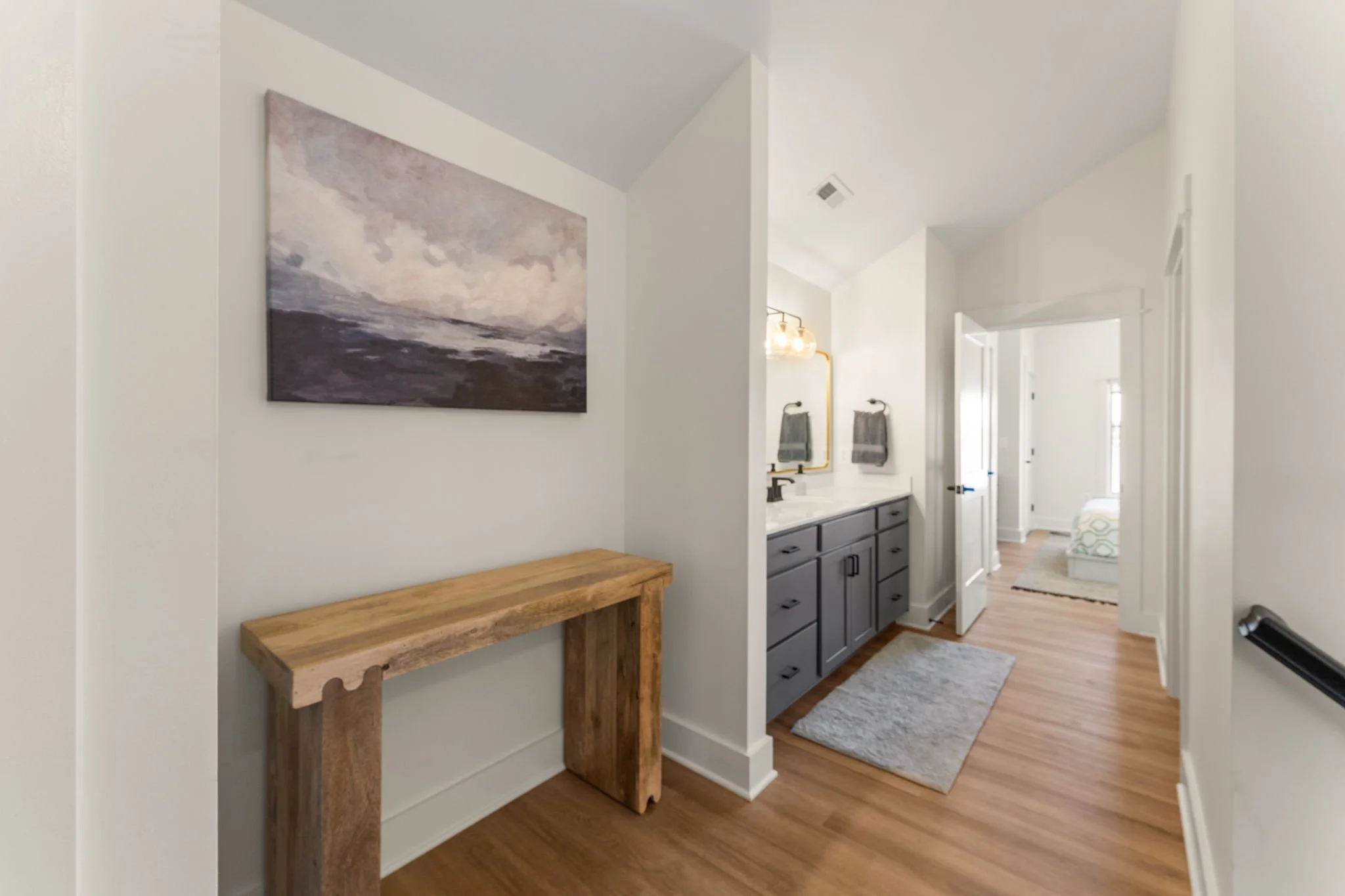 Interior view of a hallway leading to a bathroom with gray cabinets and a bedroom with a queen bed.