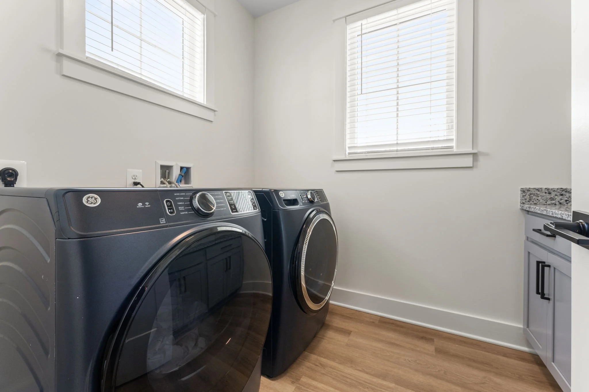 A laundry room with a front-loading washing machine and dryer, a granite countertop, and cabinets.
