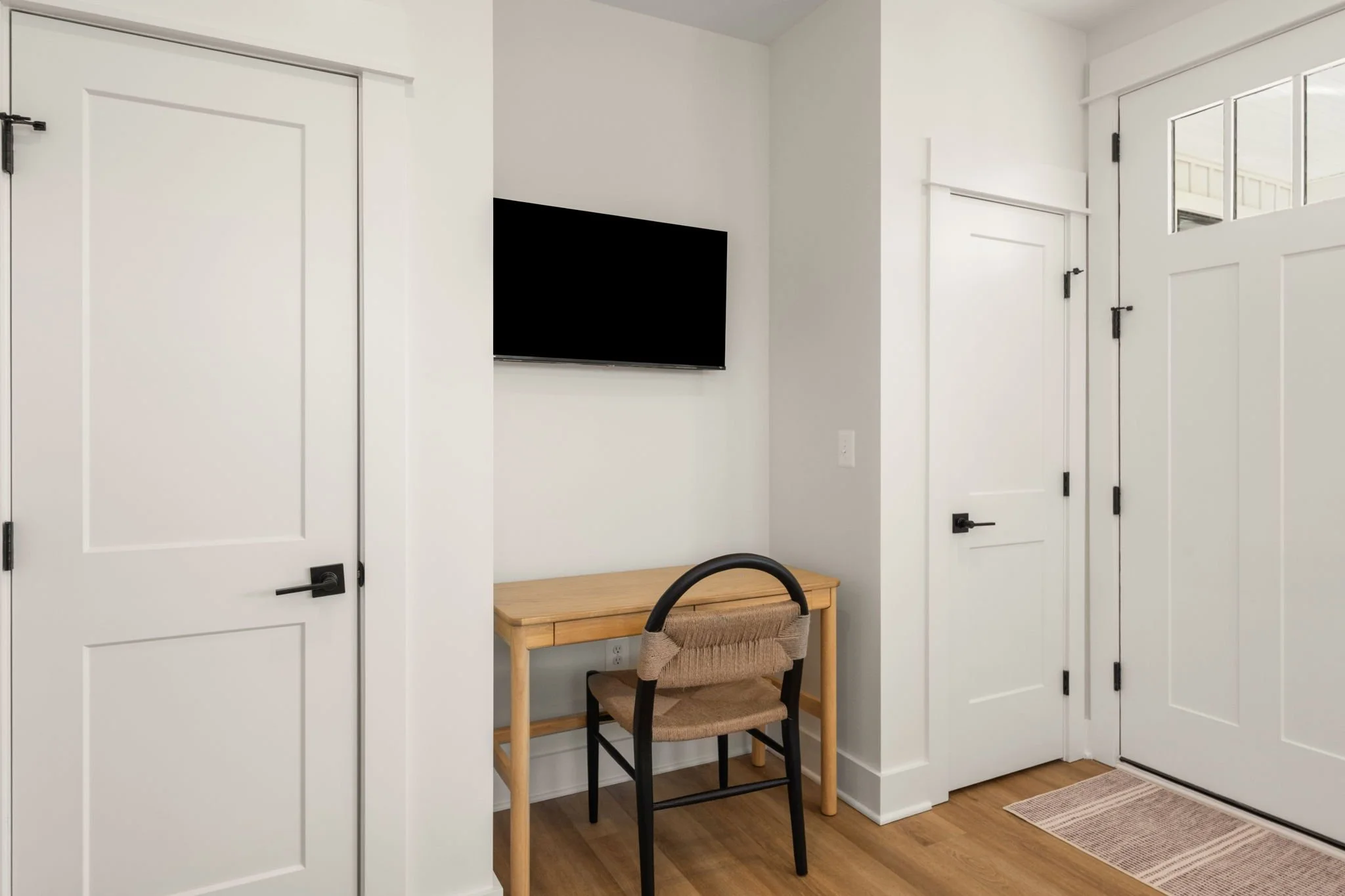 Interior view of a bedroom with white walls and doors, a wall-mounted TV, a wooden desk and chair.