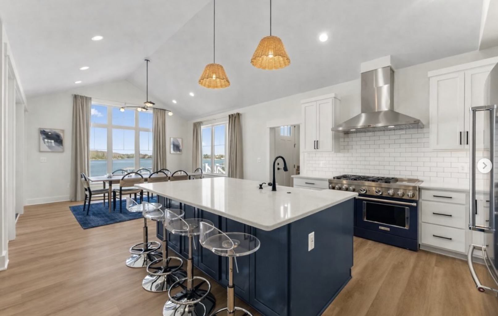 Modern kitchen and dining area with stainless steel appliances, a large island with a quartz countertop, and large windows overlooking a water view.