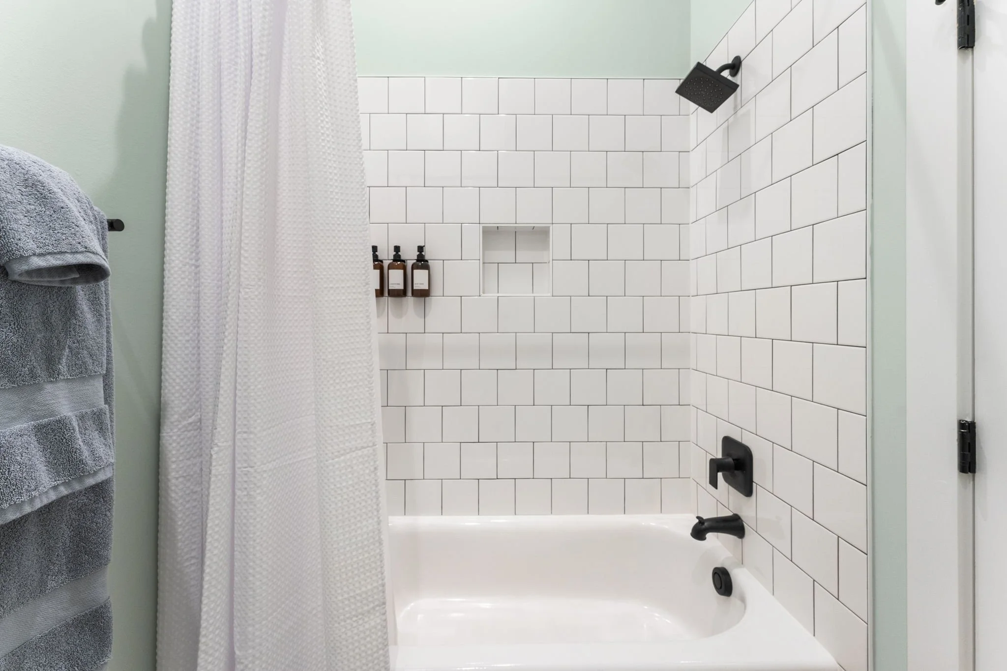 A clean bathroom shower with black fixtures and a built-in corner niche with shampoo/conditioner/soap.