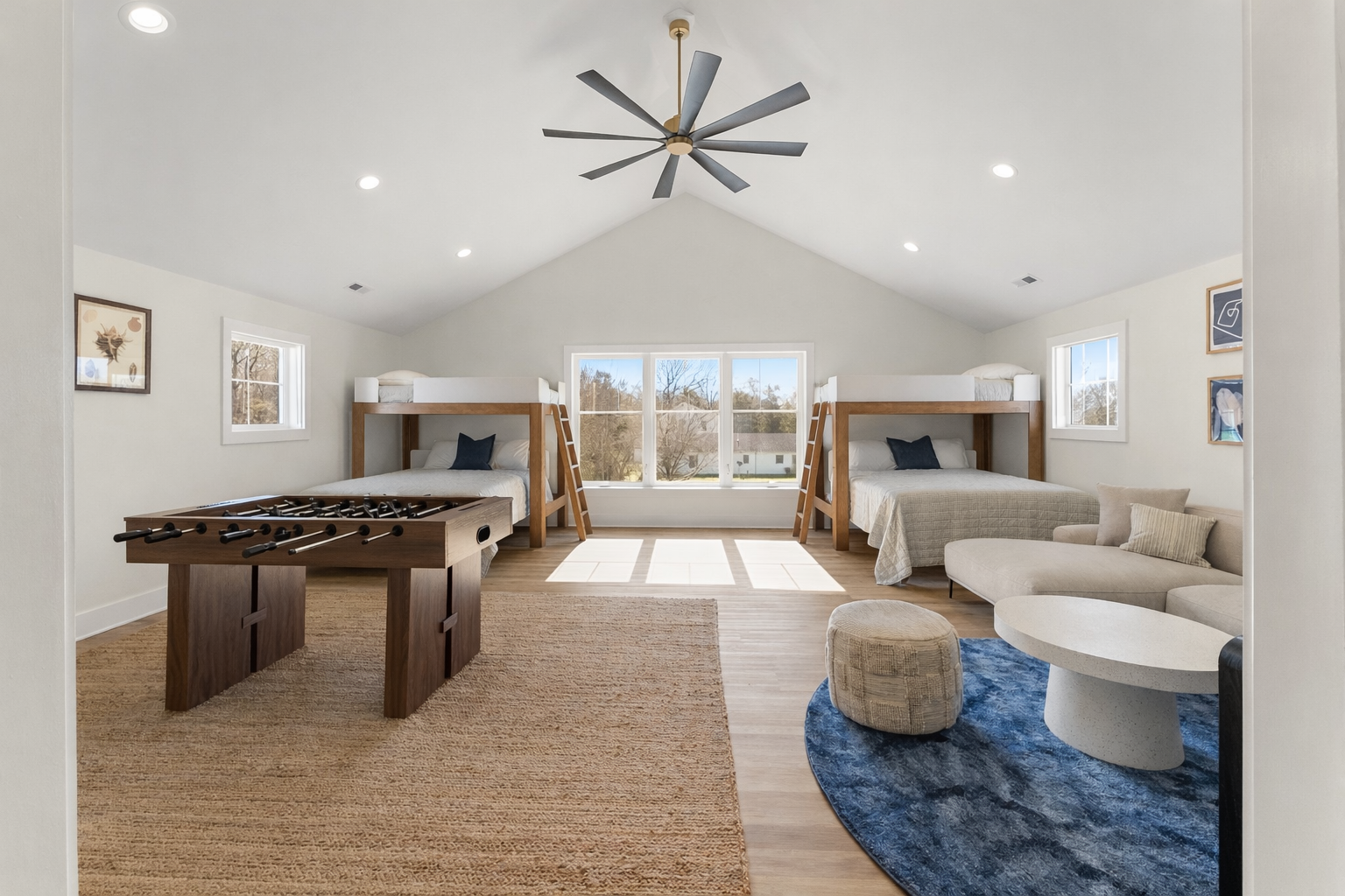 A spacious bonus rec room with two bunk beds, a foosball table, a sitting area with a sectional sofa, a coffee table, and a window overlooking the front yard.