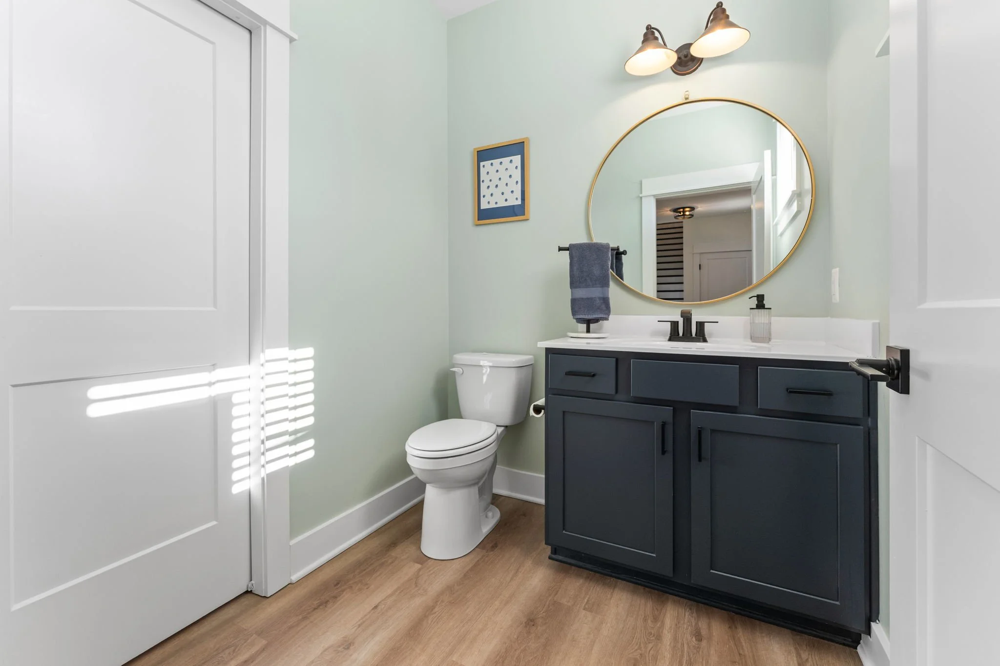 Half bathroom with a navy blue vanity, white countertop, and a round mirror above the sink.