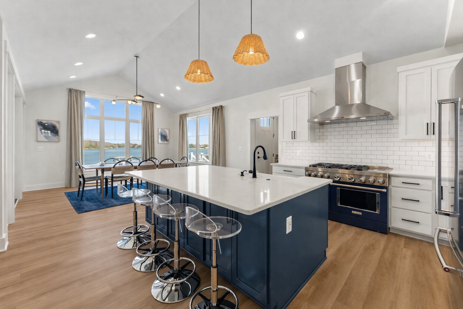 Modern kitchen and dining area with stainless steel appliances, a large island with a quartz countertop, and large windows overlooking a water view.
