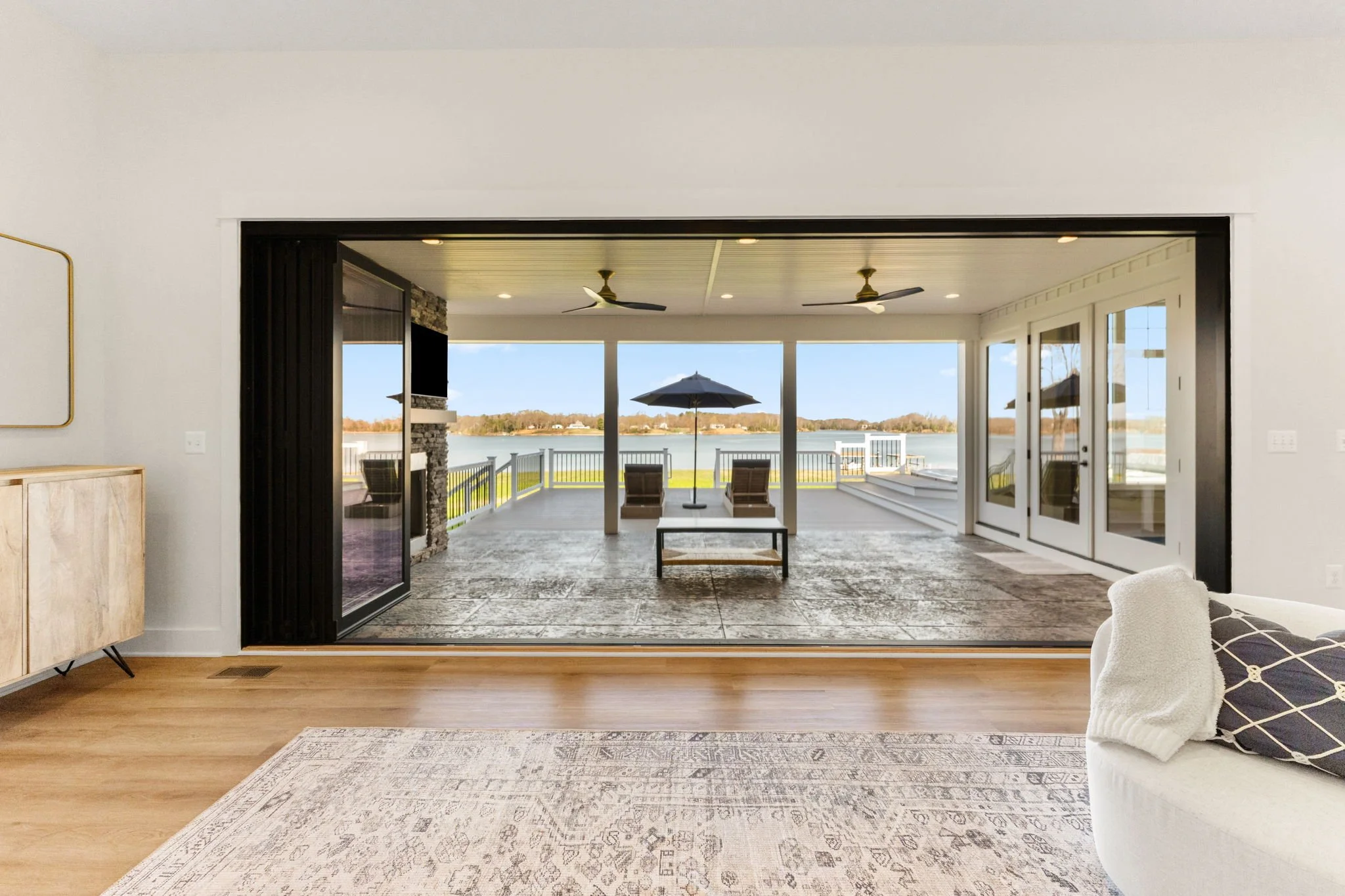 A fully collapsible sliding glass wall leading to an outdoor patio with retractable screens and a waterfront view.