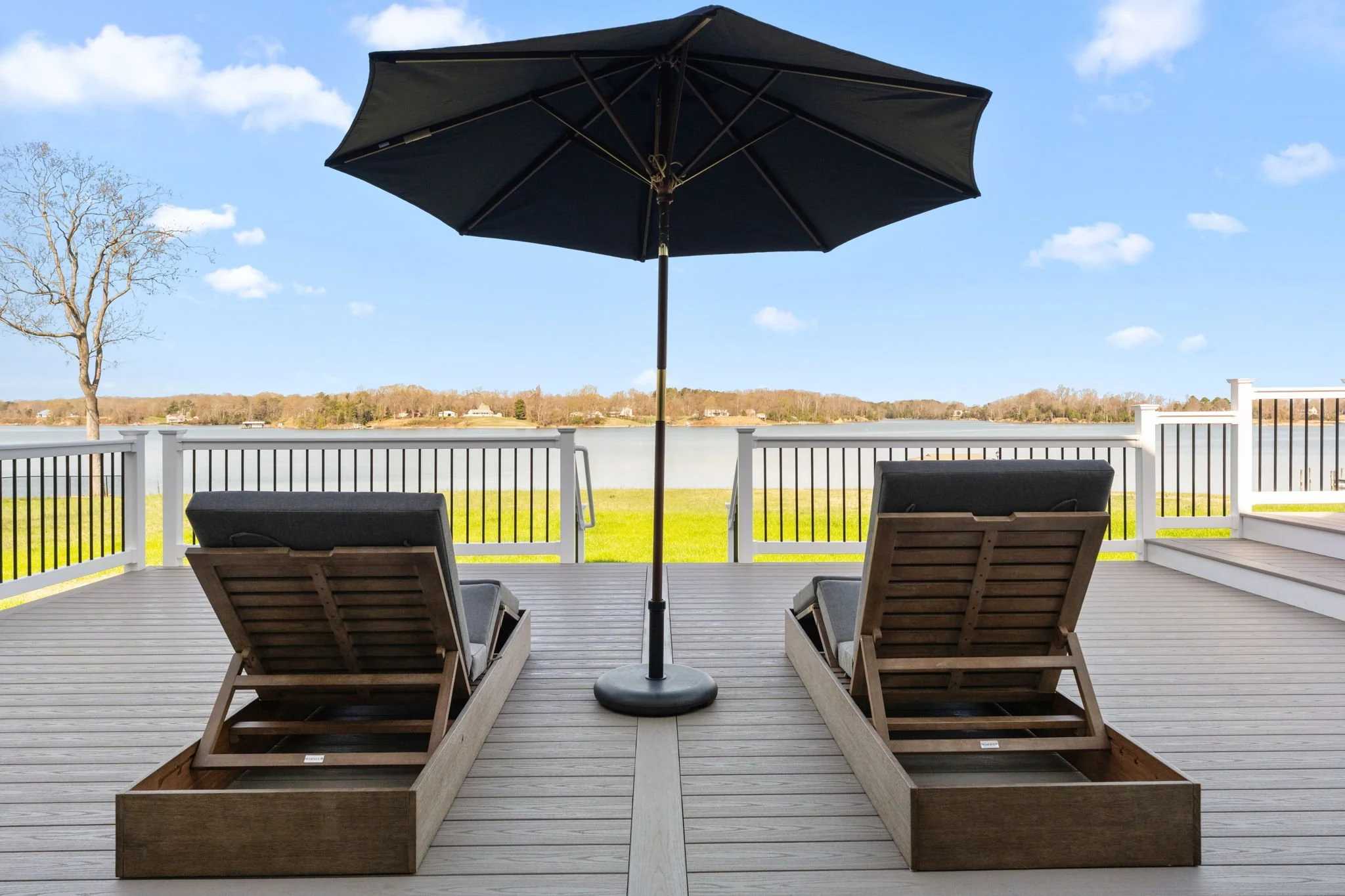 View of a backyard deck with two wooden lounge chairs and a patio umbrella overlooking the water.