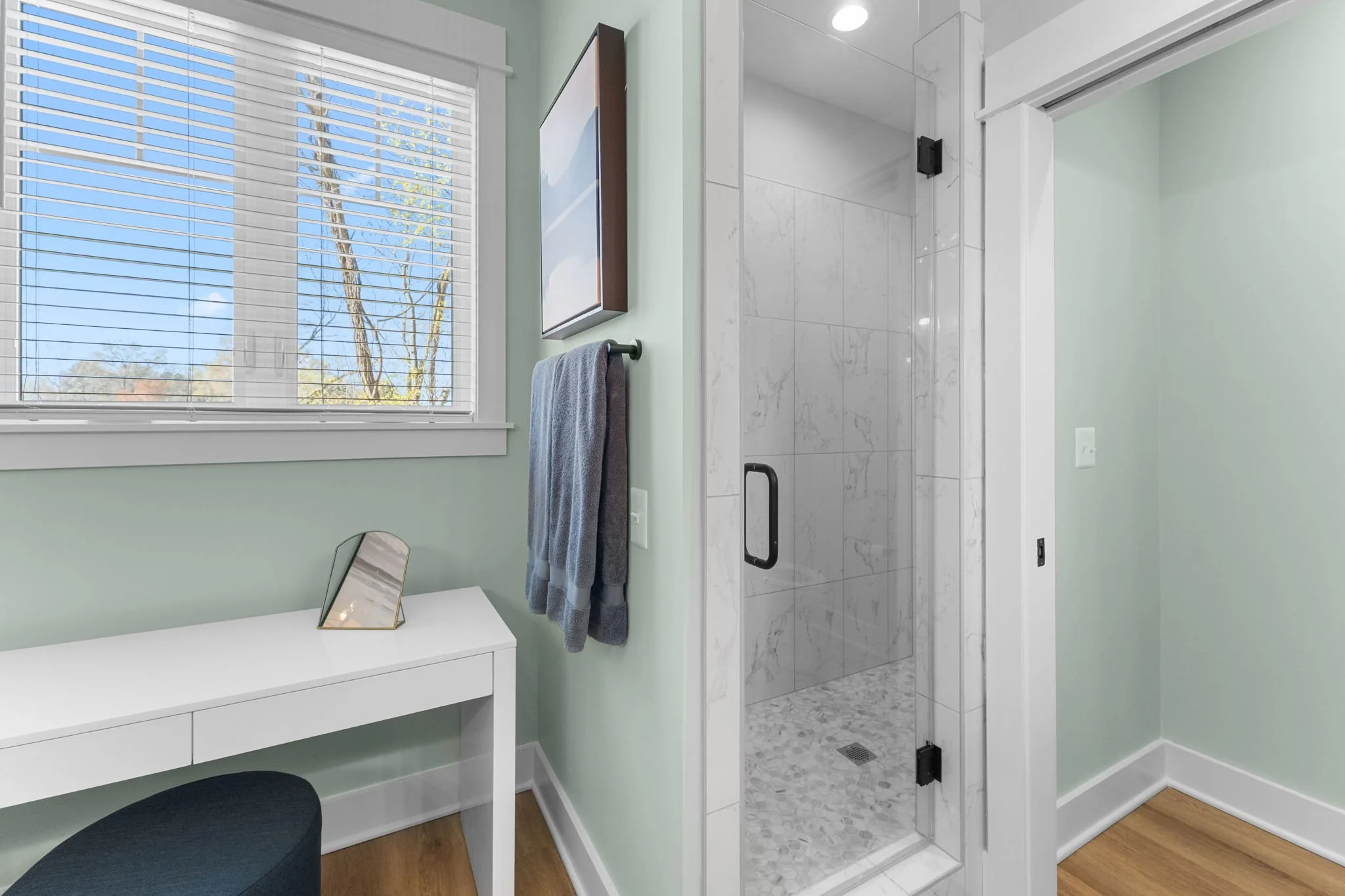 Master bathroom with a shower on the right, a white vanity below the window, and a stool.