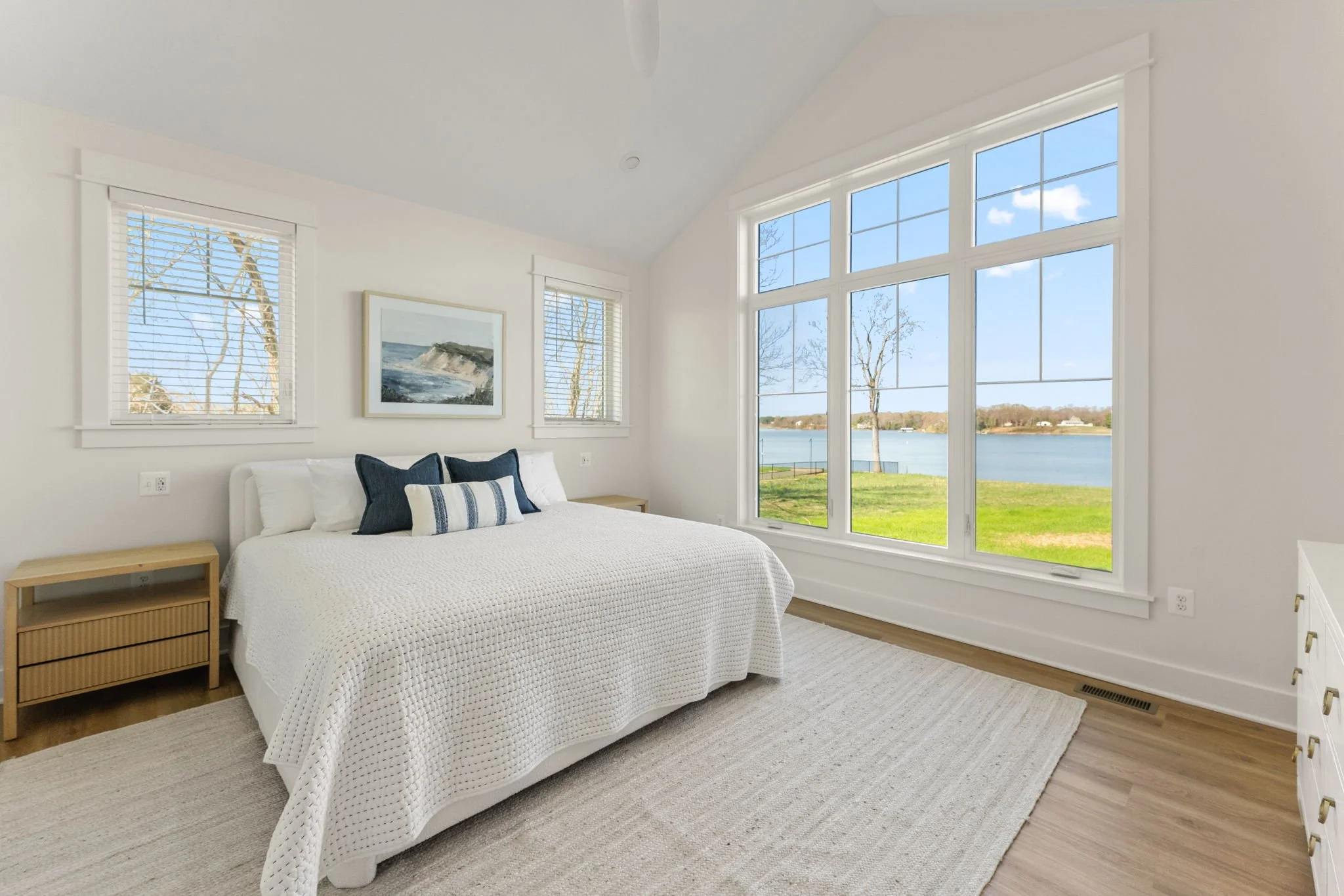Master bedroom with a large window overlooking the water, white walls, a king-sized bed, and wooden nightstands.